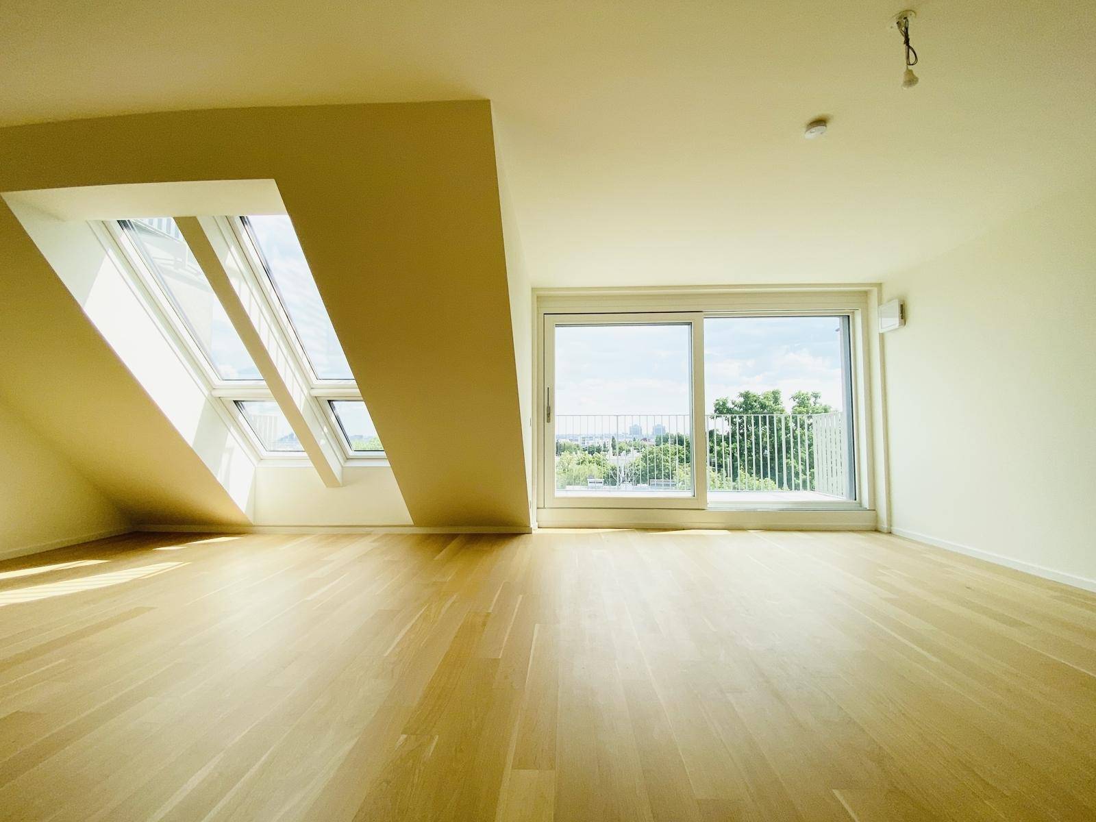 Helles Zimmer mit Holzboden, Dachfenstern und Zugang zu einem Balkon mit Weitblick.