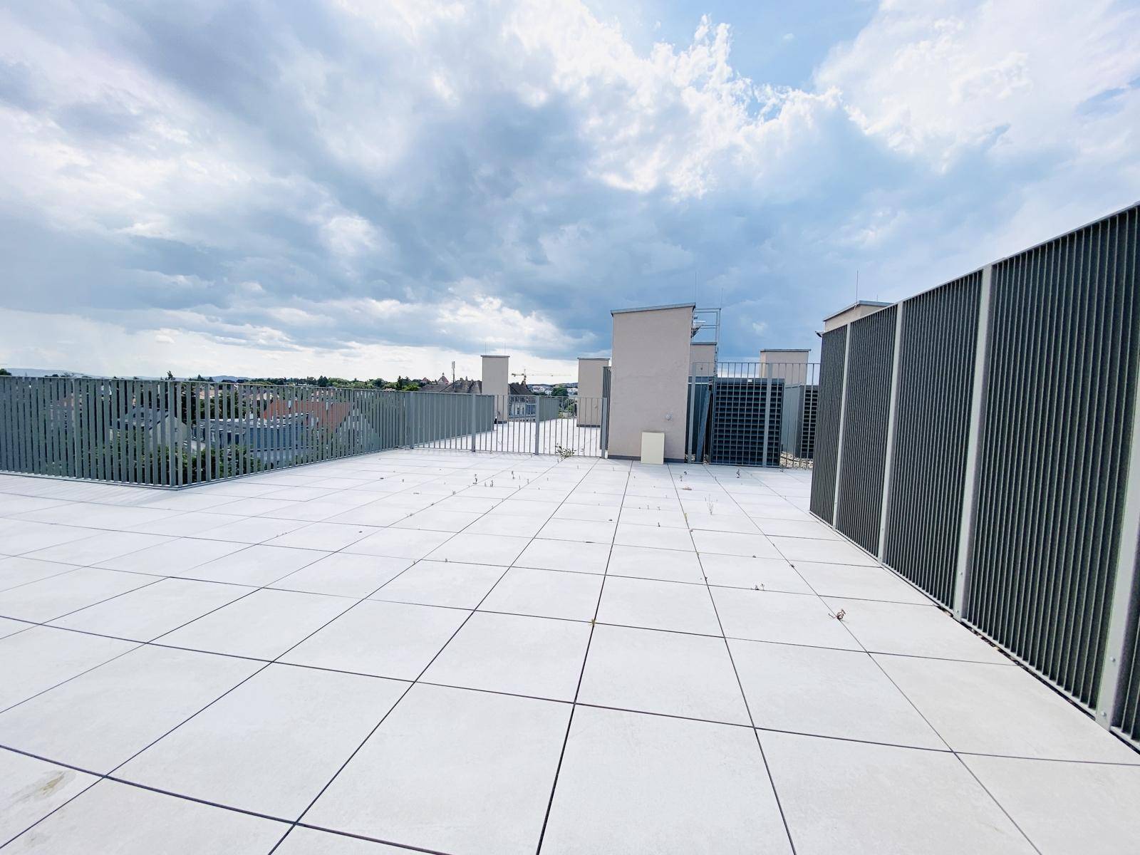Weitläufige Dachterrasse mit Fliesenboden und Blick auf die umliegenden Gebäude und den Himmel.