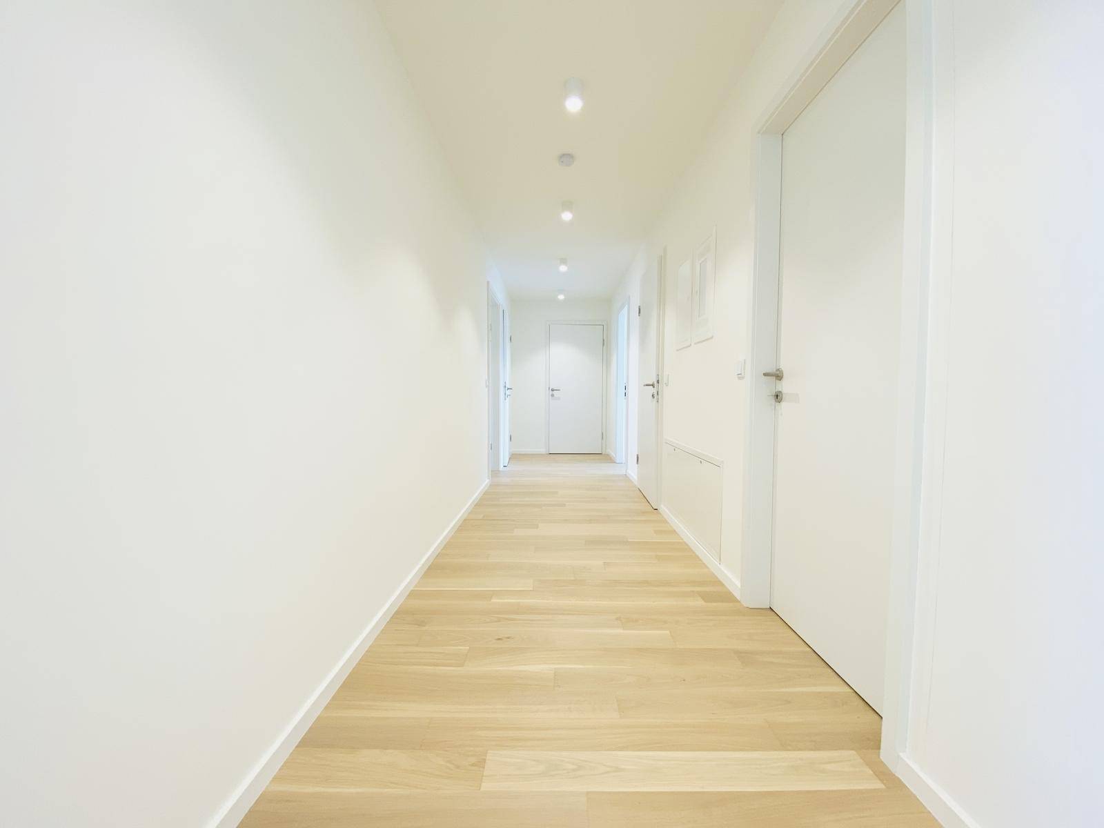 Langer, heller Flur mit Holzboden und weißen Türen, führt zu verschiedenen Räumen der Wohnung.