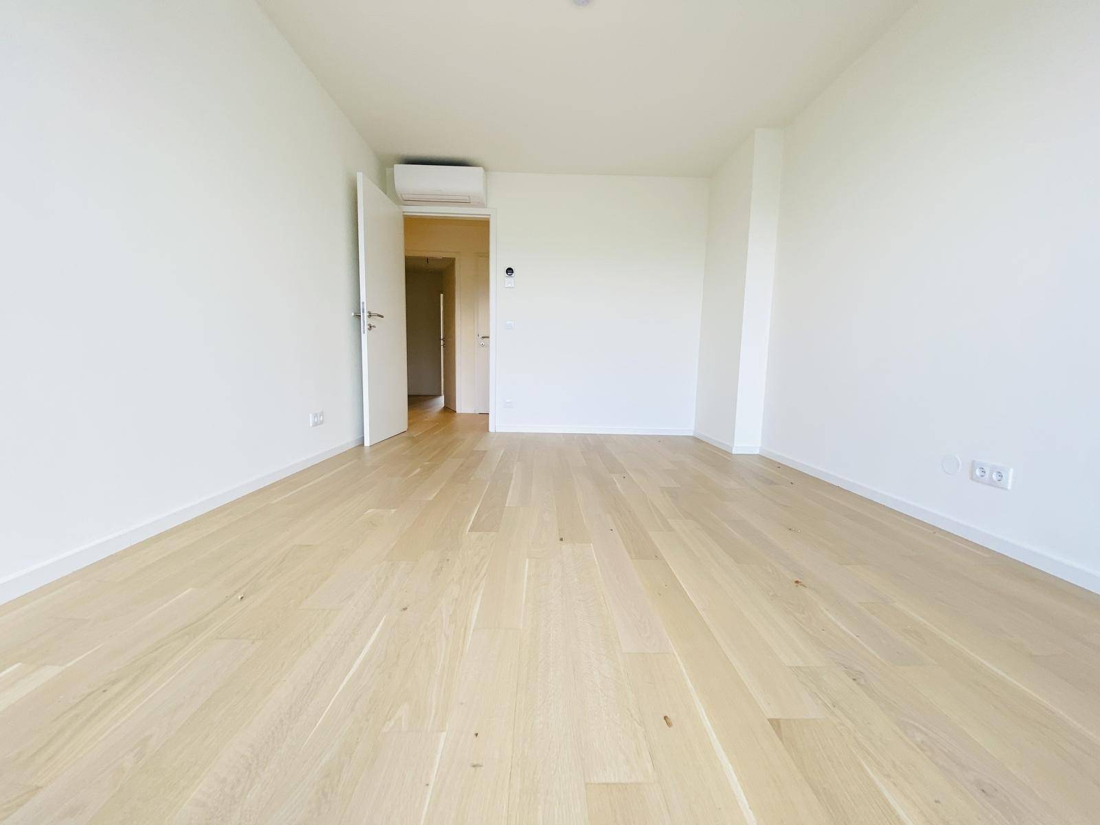 Heller, leerer Raum mit Holzboden und Klimaanlage, bereit zur individuellen Gestaltung.