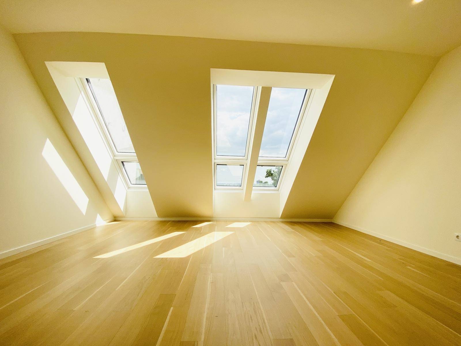 Geräumiger Dachgeschossraum mit Holzboden und mehreren Dachfenstern für viel Tageslicht.