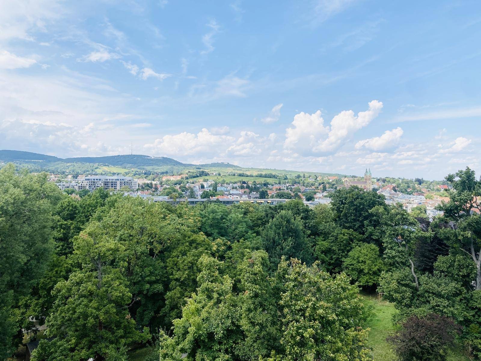 Panoramablick über eine grüne Stadtlandschaft mit Hügeln und weitem Horizont.
