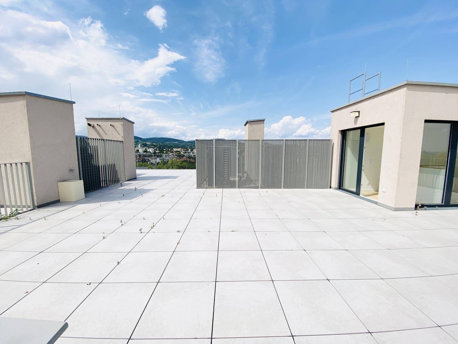 Weitläufige Dachterrasse mit Fliesenboden und Blick auf die umliegenden Gebäude unter blauem Himmel.