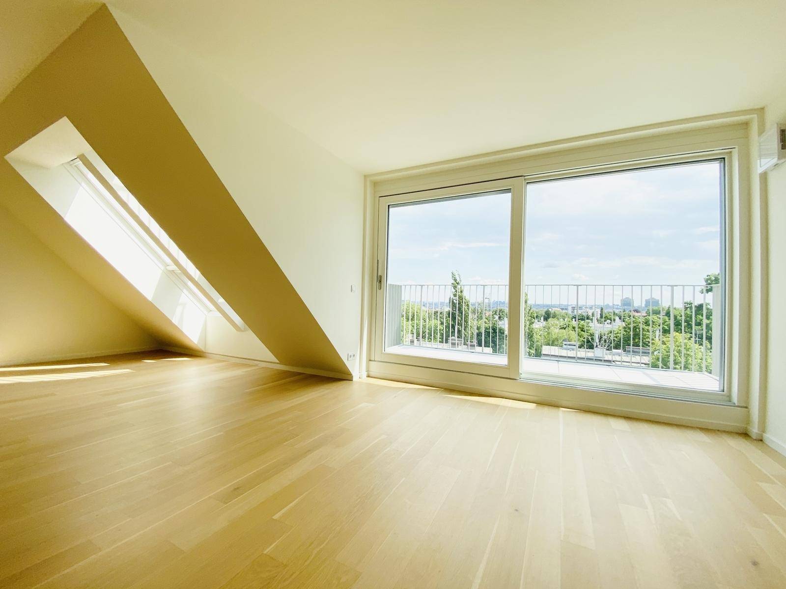 Lichtdurchfluteter Wohnraum mit Schiebetür zum Balkon und schrägem Dachfenster, bietet weite Aussicht.