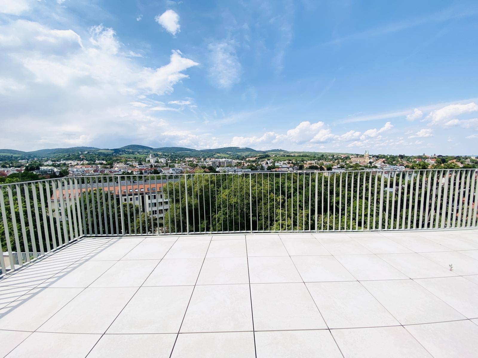 Sonniger Dachterrassenbereich mit Fliesen und weitem Blick über die Stadt und die grünen Hügel.