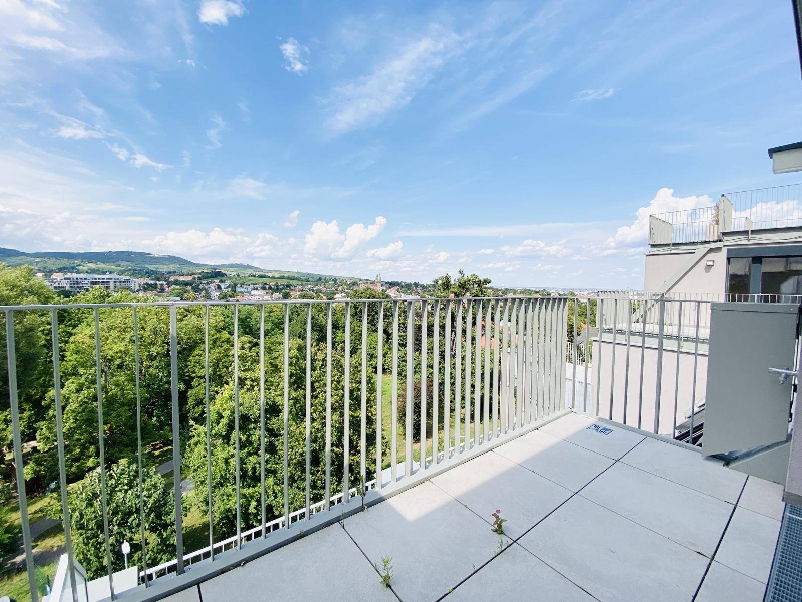Geräumiger Balkon mit Fliesenboden und Metallgeländer, bietet einen weiten Blick ins Grüne.