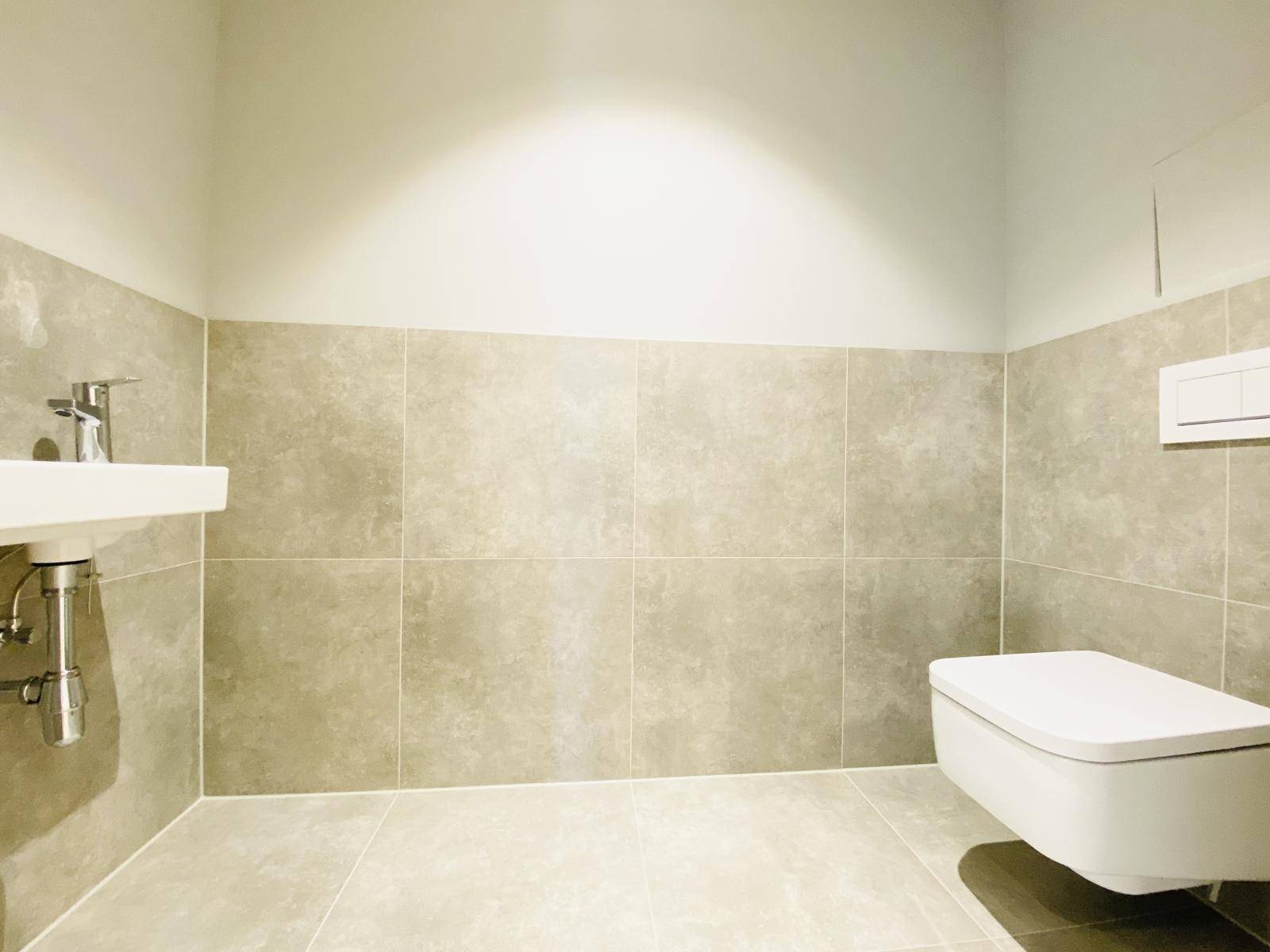 Modernes Gäste-WC mit hellgrauen Fliesen, wandhängender Toilette und kleinem Waschbecken.