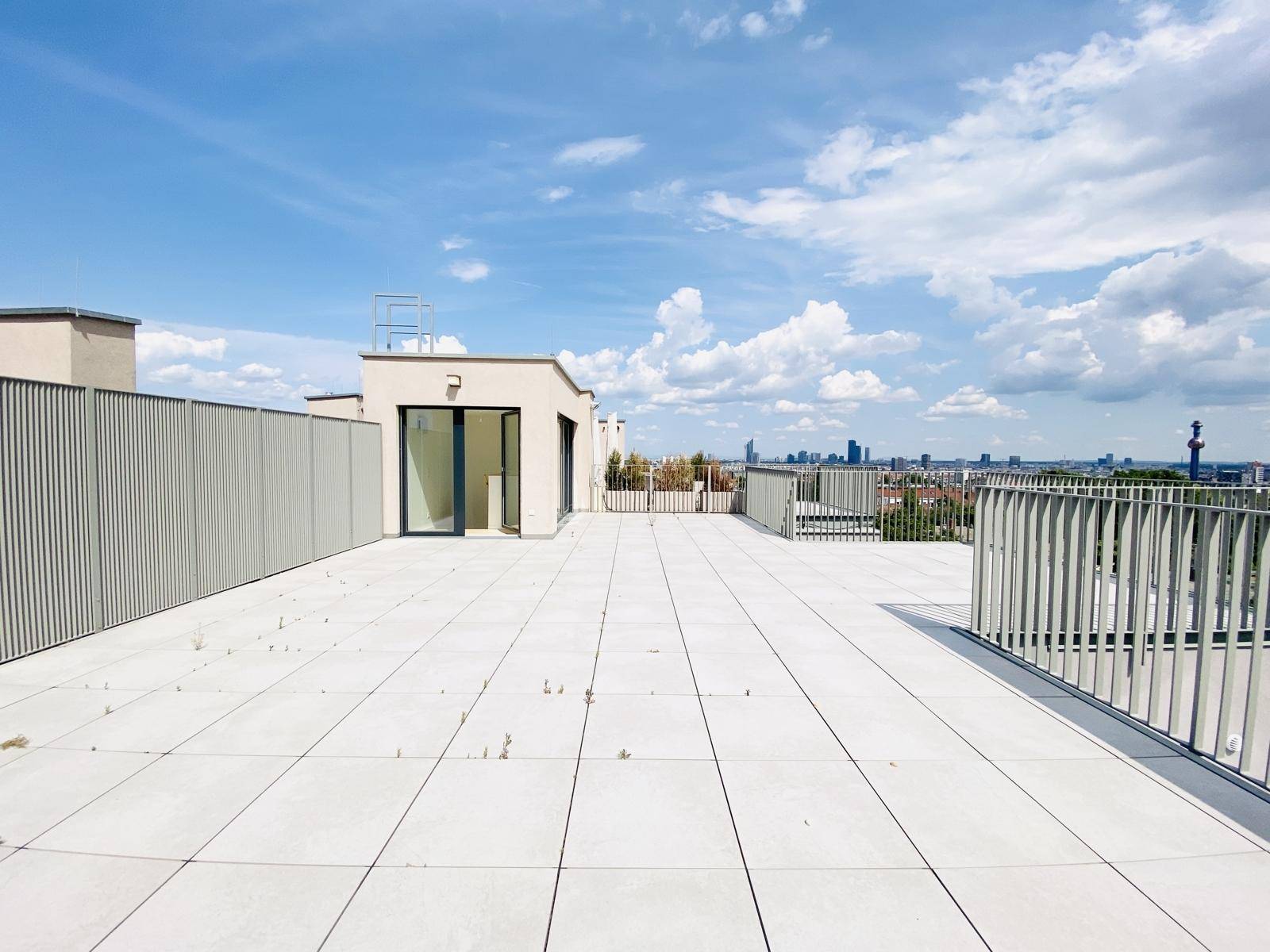 Große Dachterrasse mit Fliesenboden und weitem Blick auf die Stadtkulisse unter klarem Himmel.