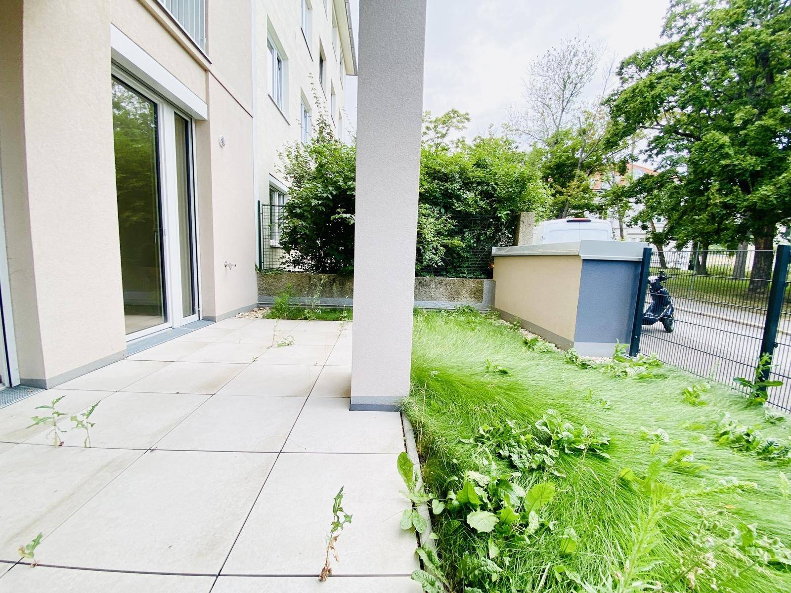 Terrasse mit Fliesenboden und angrenzendem, noch ungestaltetem Grünstreifen am Gebäude.