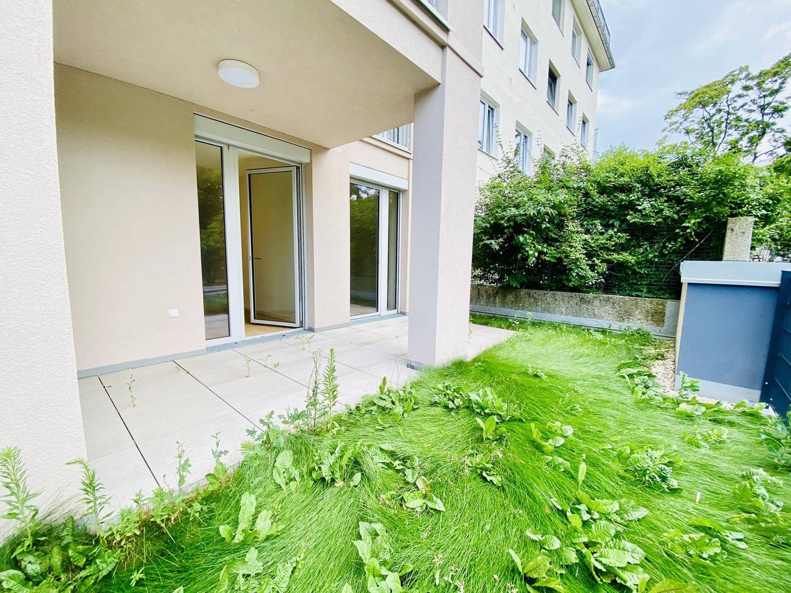 Erdgeschoss-Terrasse mit Fliesen und einem schmalen Rasenstreifen, der zum Garten führt.
