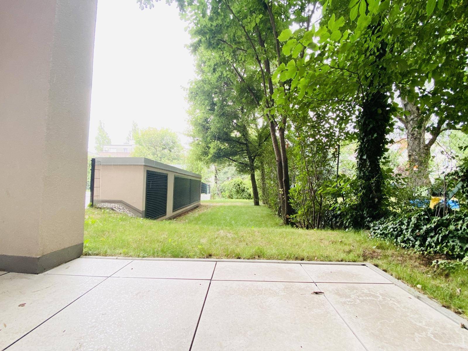 Blick von der Terrasse auf den grünen Gartenbereich mit Bäumen und Sträuchern.
