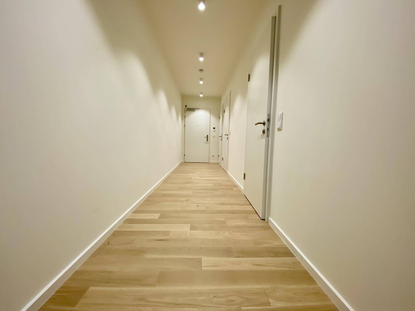 Langer, heller Flur mit Parkettboden und modernen Einbaustrahlern an der Decke.