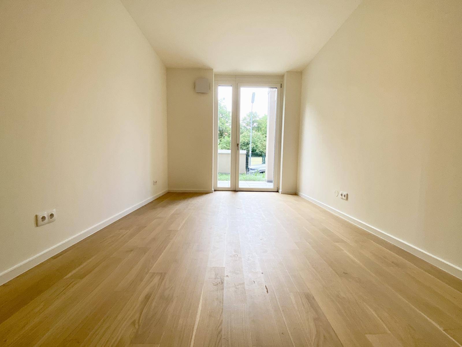 Geräumiges Schlafzimmer mit hellem Parkett und Zugang zu einem kleinen Außenbereich.