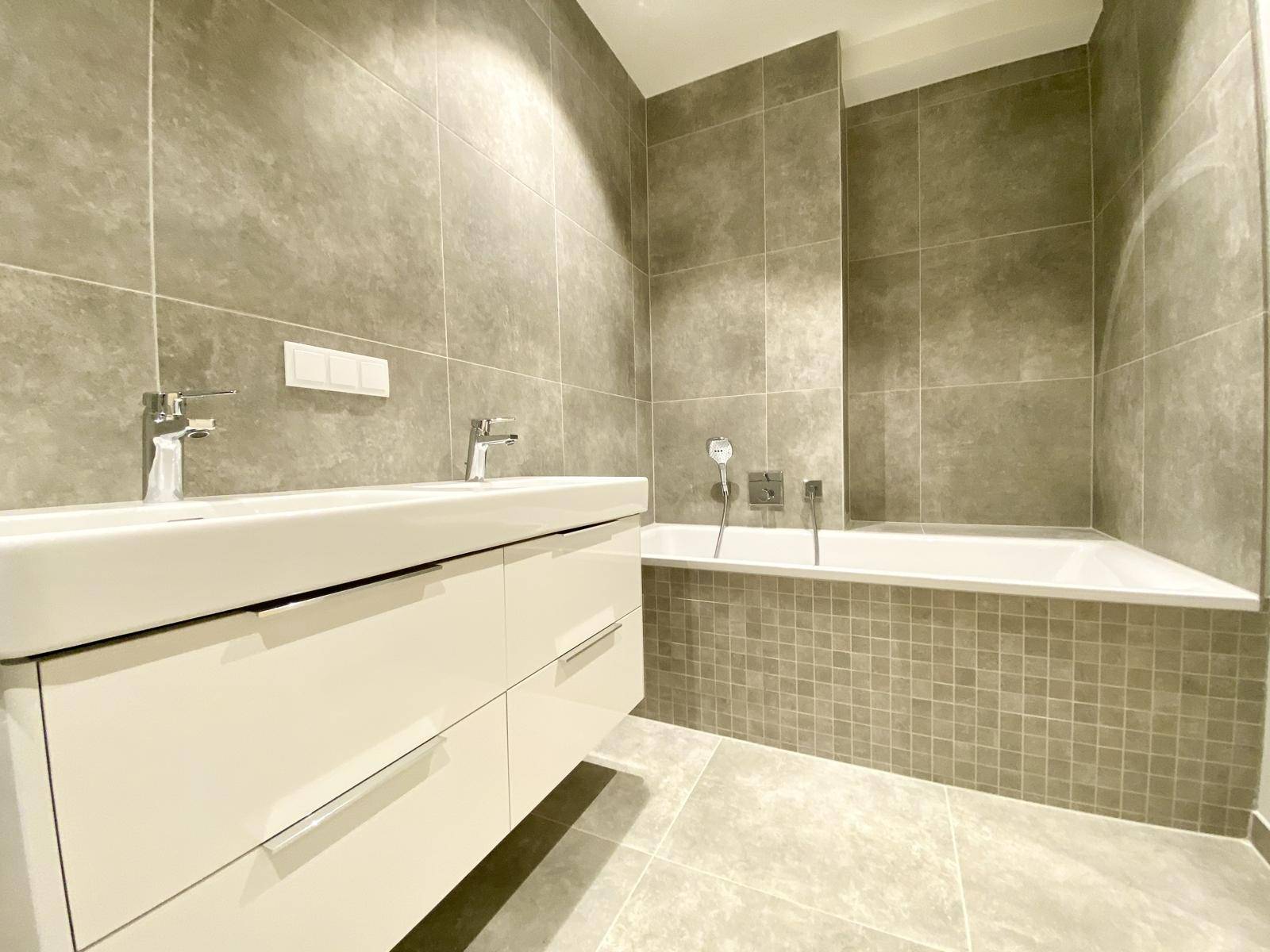 Elegantes Badezimmer mit grauen Fliesen, integrierter Badewanne und modernem Doppelwaschbecken.
