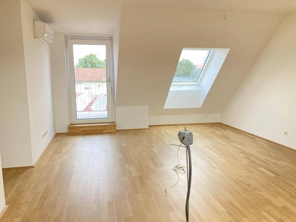 Geräumiger Dachgeschossraum mit Zugang zu einem Außenbereich, Dachfenster und Klimaanlage.