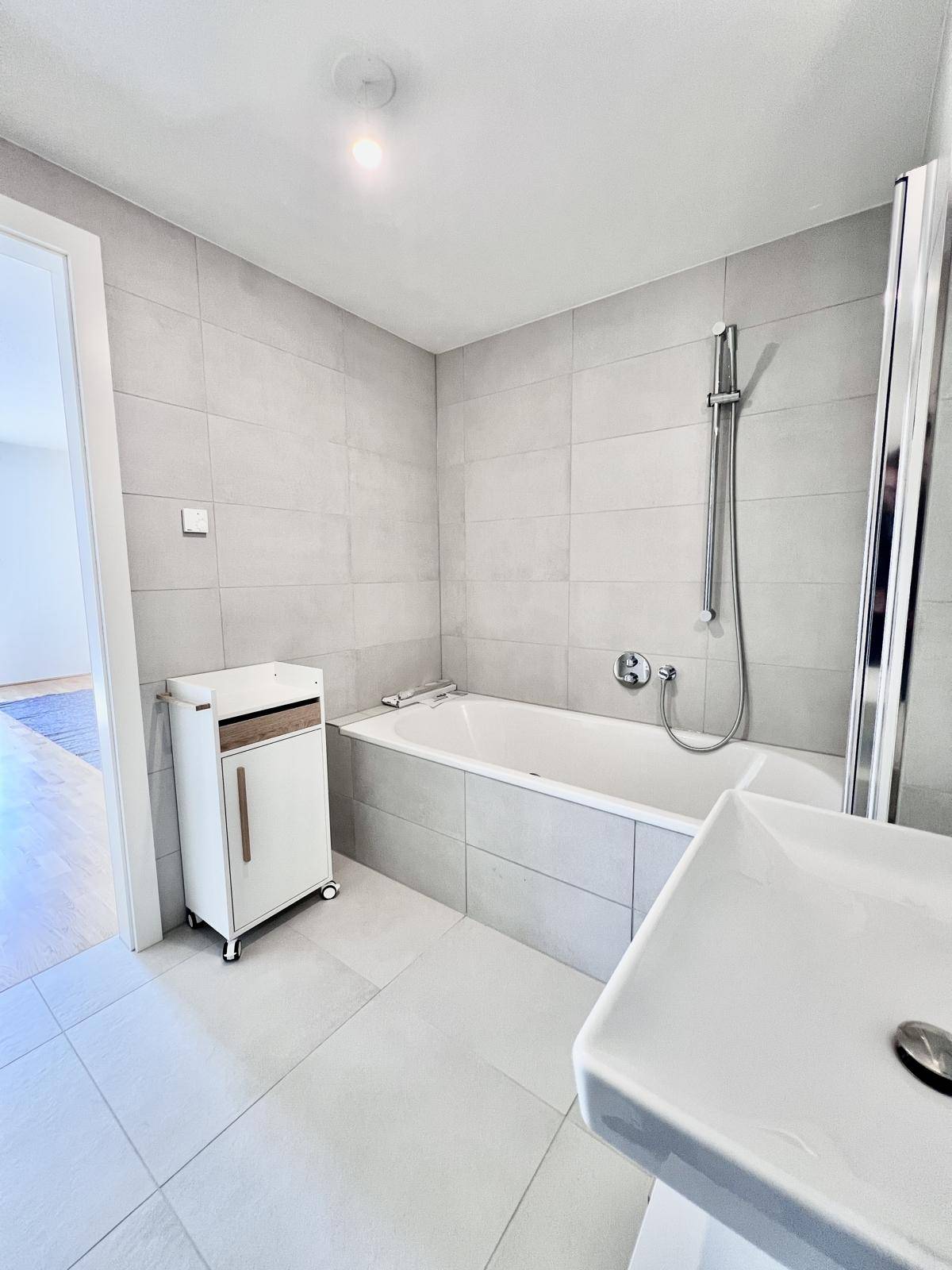 Helles Badezimmer mit Badewanne, modernem Waschtisch und grauen Fliesen.