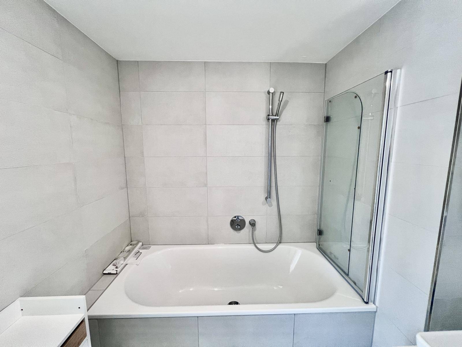 Eingebaute Badewanne mit Duscharmatur und Glasabtrennung in modernem Bad.