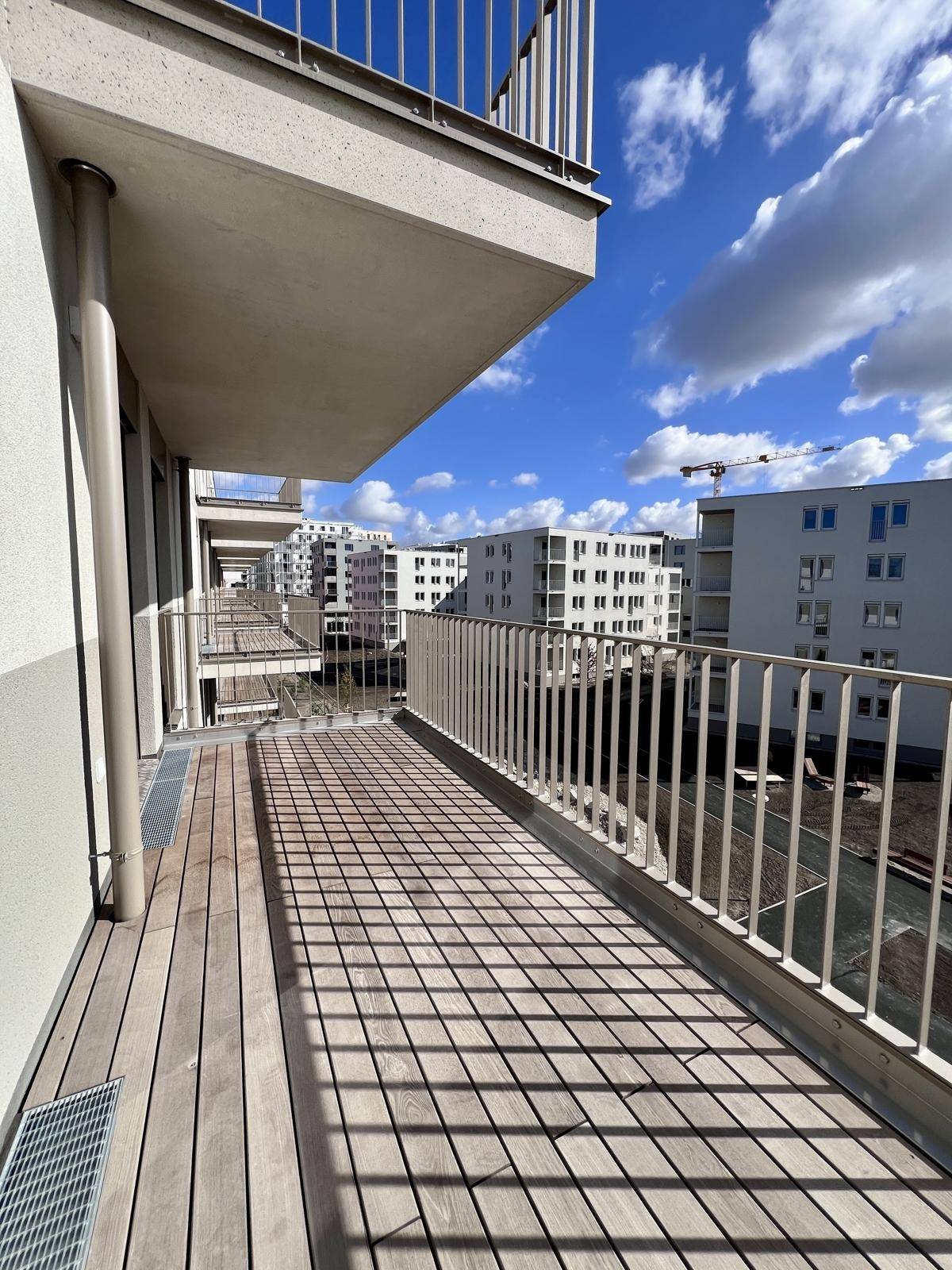 Langer Balkon mit Holzdielen und Blick auf die moderne Wohnanlage.
