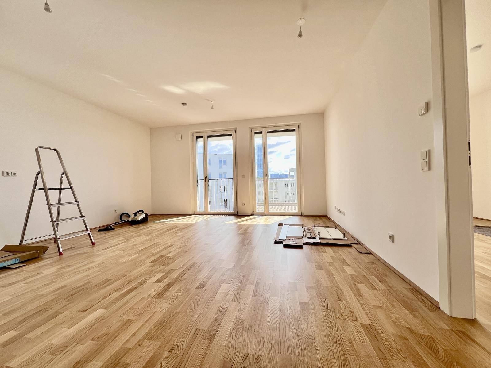 Lichtdurchfluteter Wohnbereich mit Eichenparkett und Zugang zu einem Balkon.