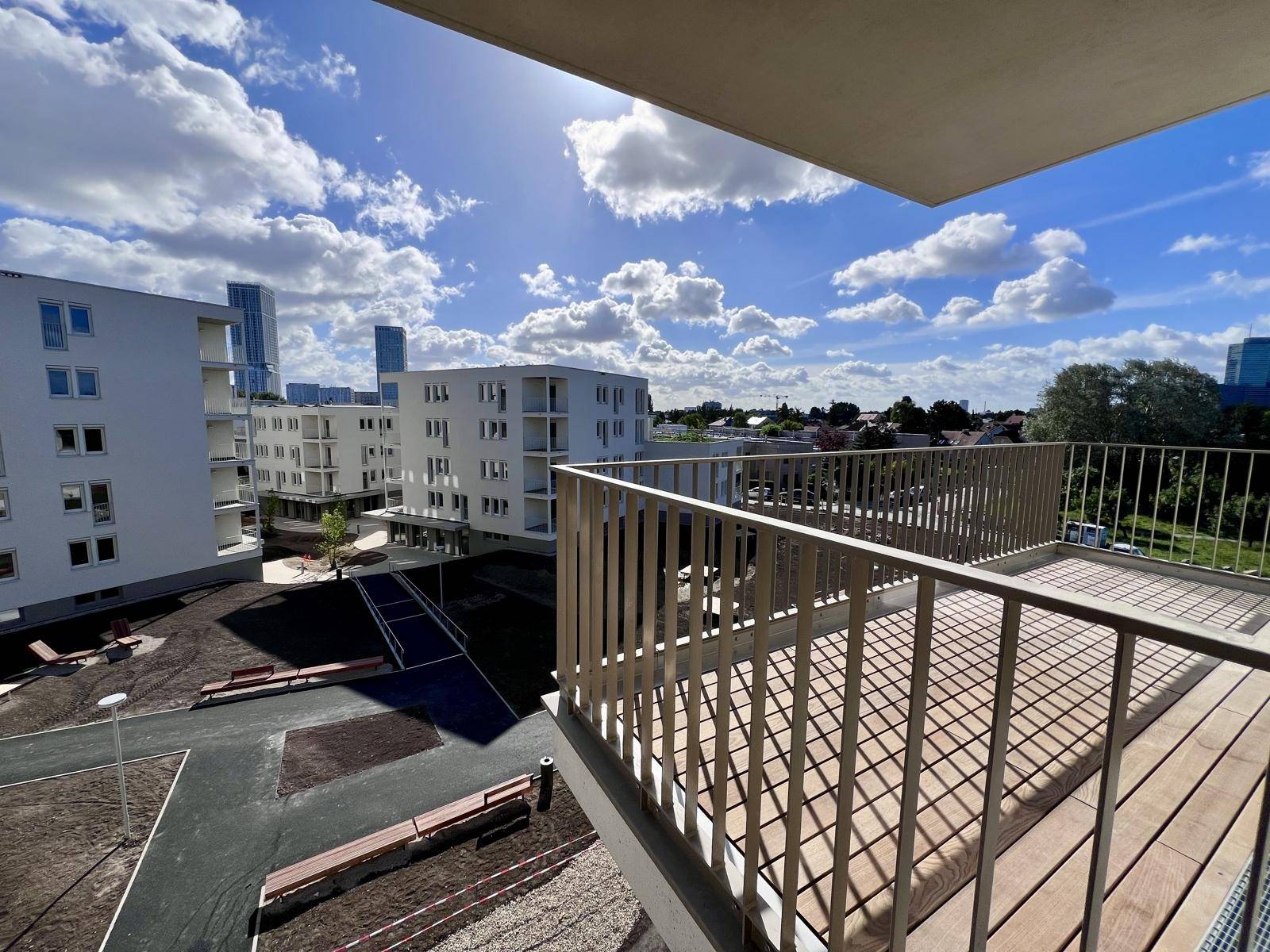Geräumiger Balkon mit Holzboden und Ausblick auf die umliegenden Neubauten.