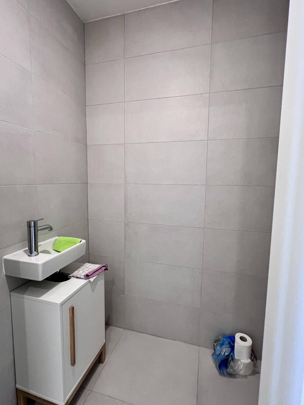 Kleines Gäste-WC mit Waschtisch und grauen Wand- und Bodenfliesen.