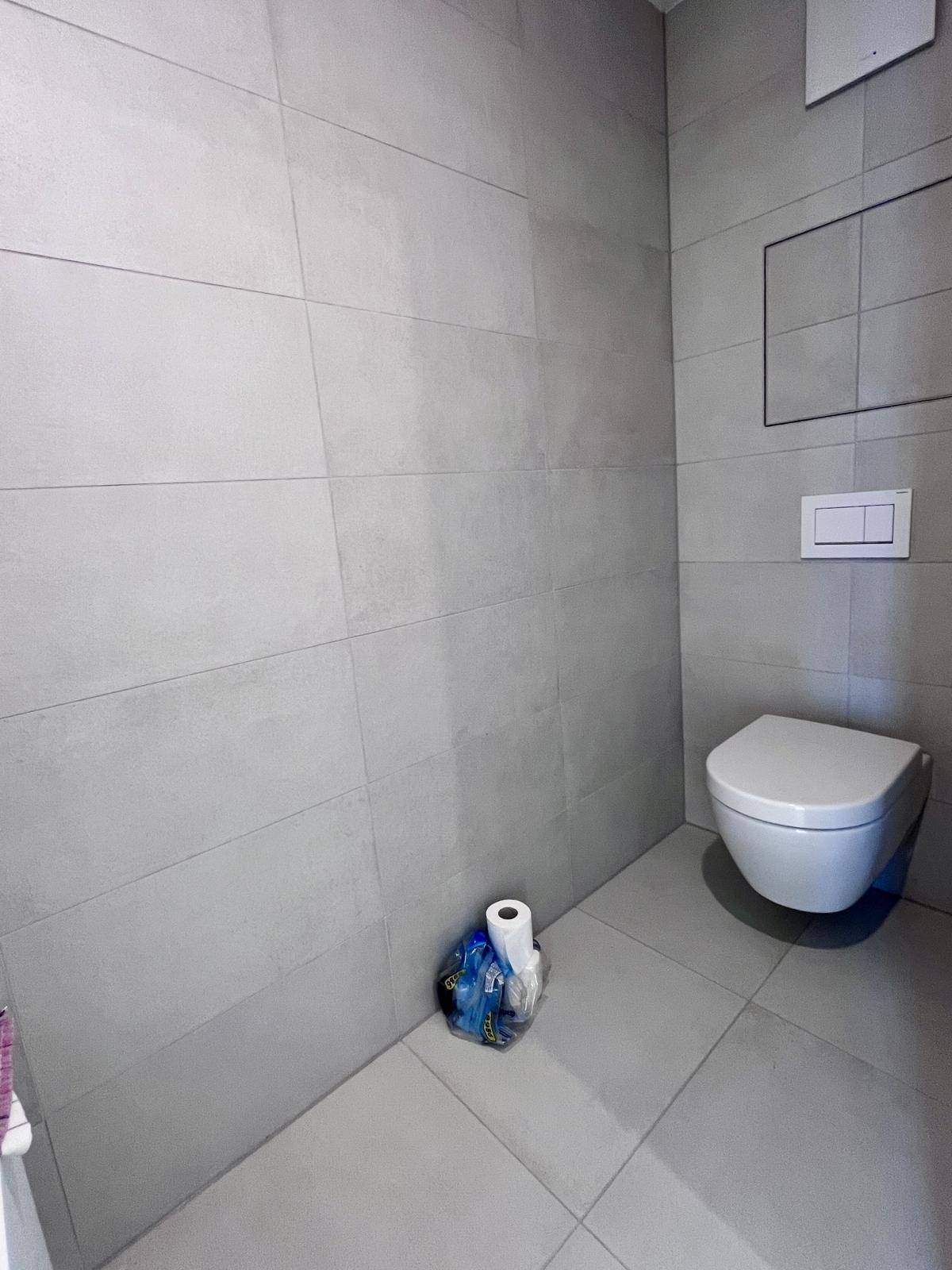 Separates WC mit wandhängender Toilette und modernen grauen Fliesen.