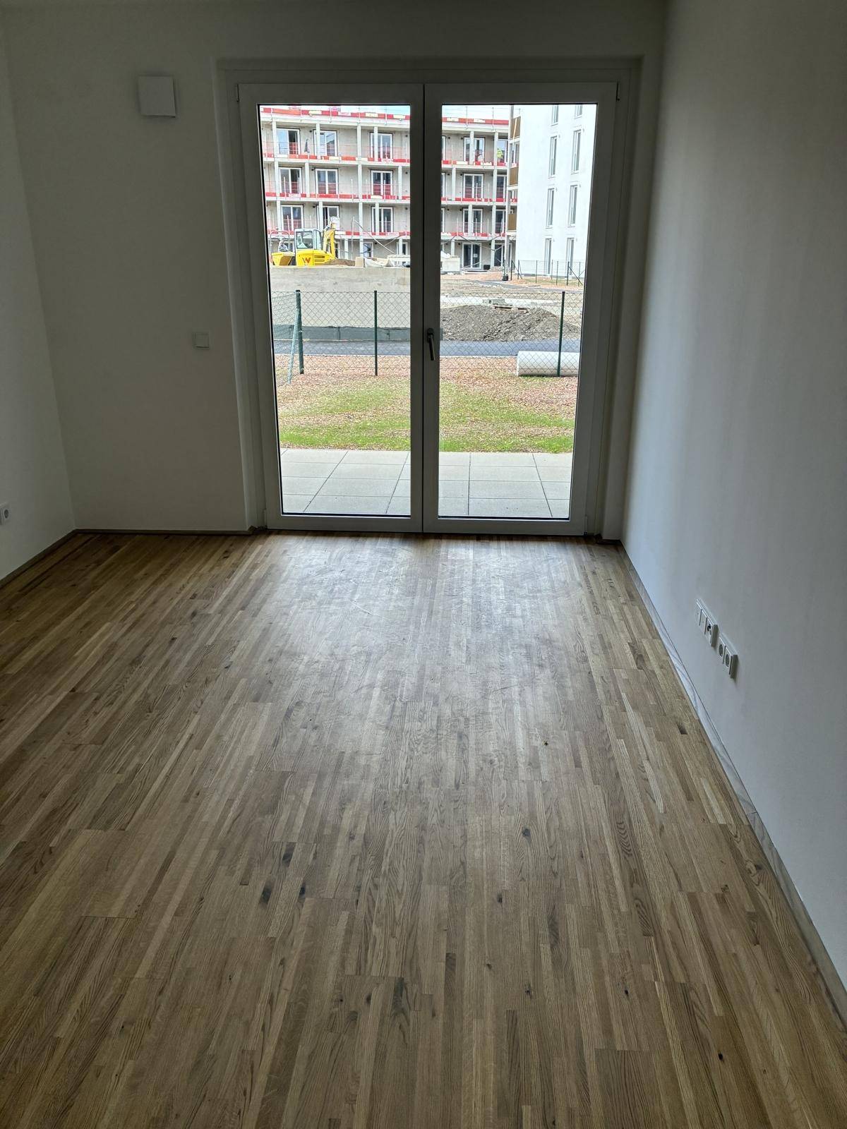 Detailansicht des Parkettbodens und der großen Fensterfront mit Blick ins Grüne.