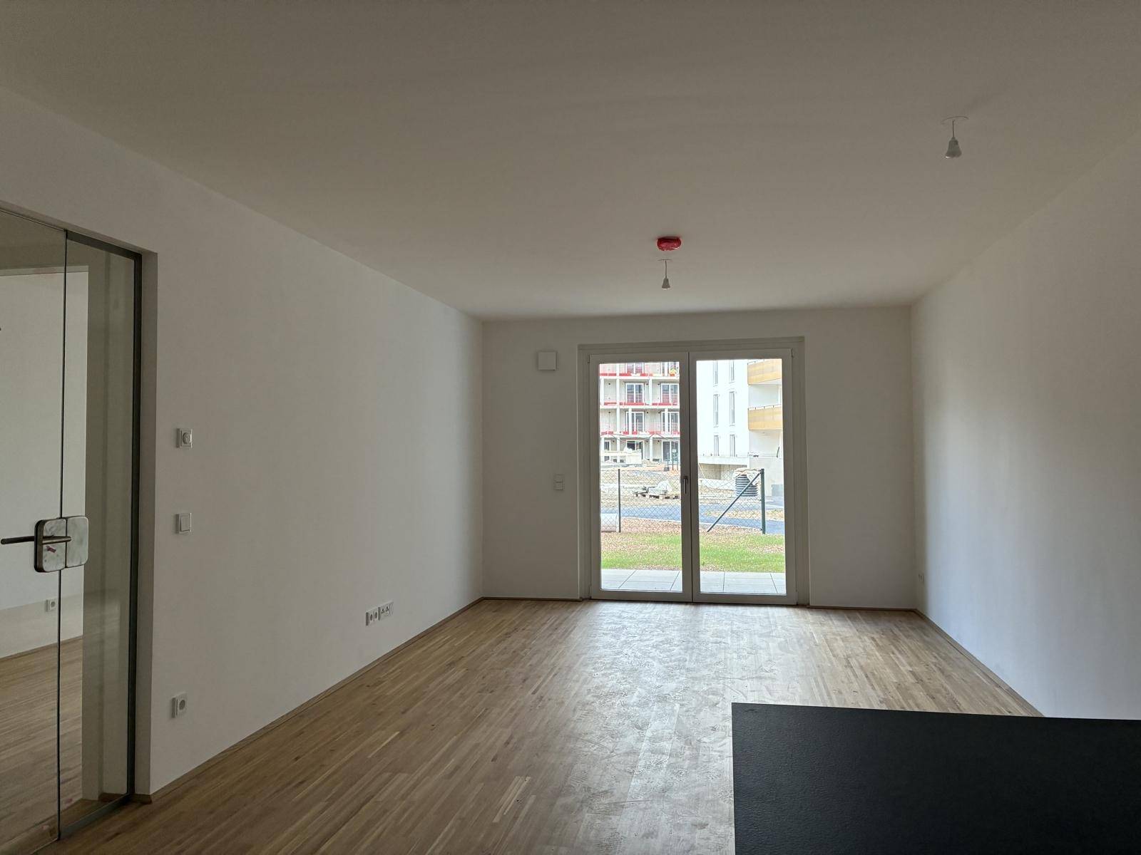 Geräumiger Wohnbereich mit Parkettboden und Blick auf die offene Küchenzeile.