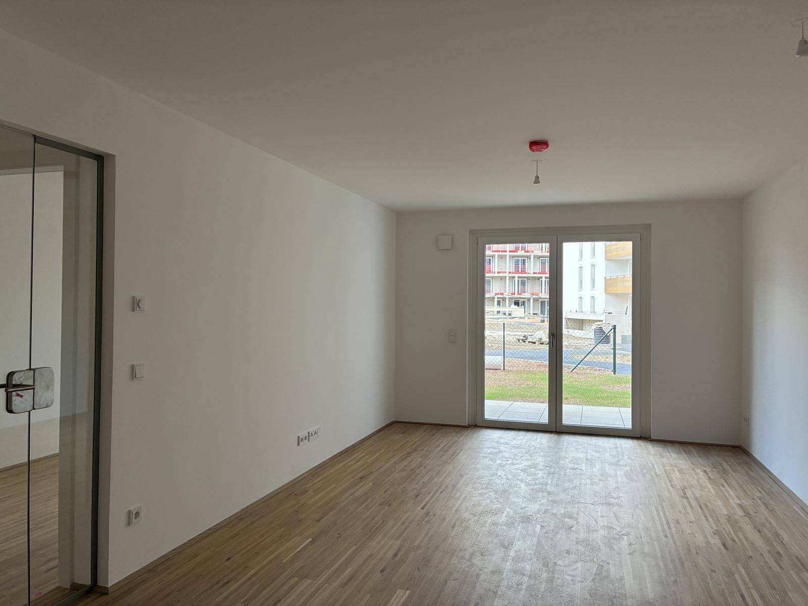 Helles Zimmer mit Parkettboden und großer Schiebetür zum Außenbereich.