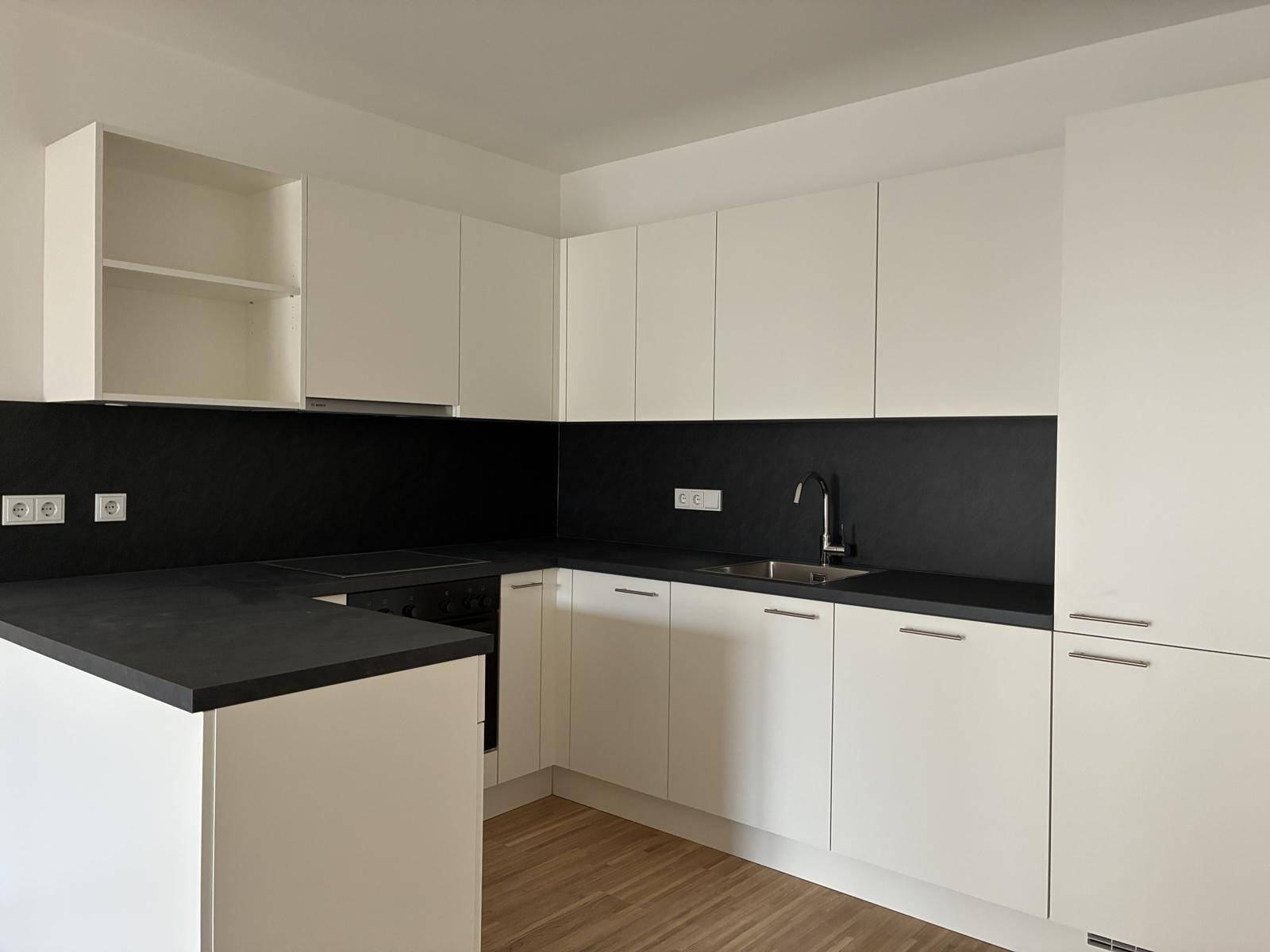 Moderne Einbauküche mit weißen Schränken, dunkler Arbeitsplatte und integrierten Geräten.