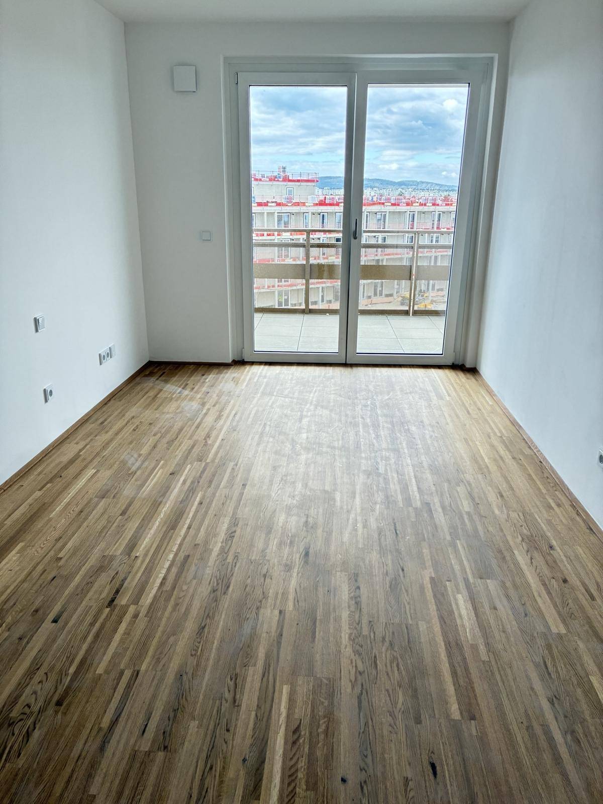 Helles Schlafzimmer mit Parkettboden und großem Fenster, das einen weiten Blick über die Stadt ermöglicht.