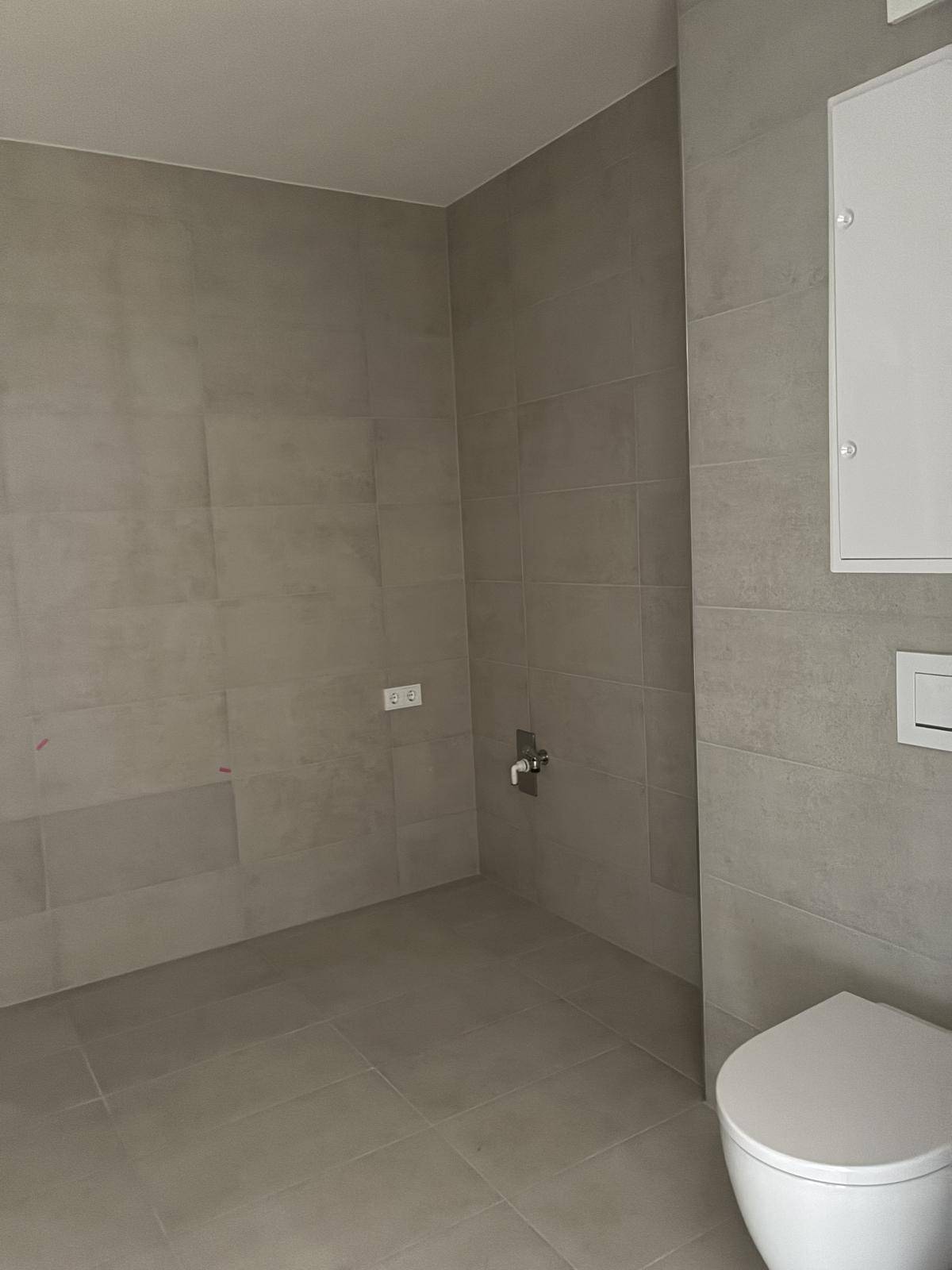 Gefliestes WC mit wandmontierter Toilette und ausreichend Platz für zusätzliche Badmöbel.