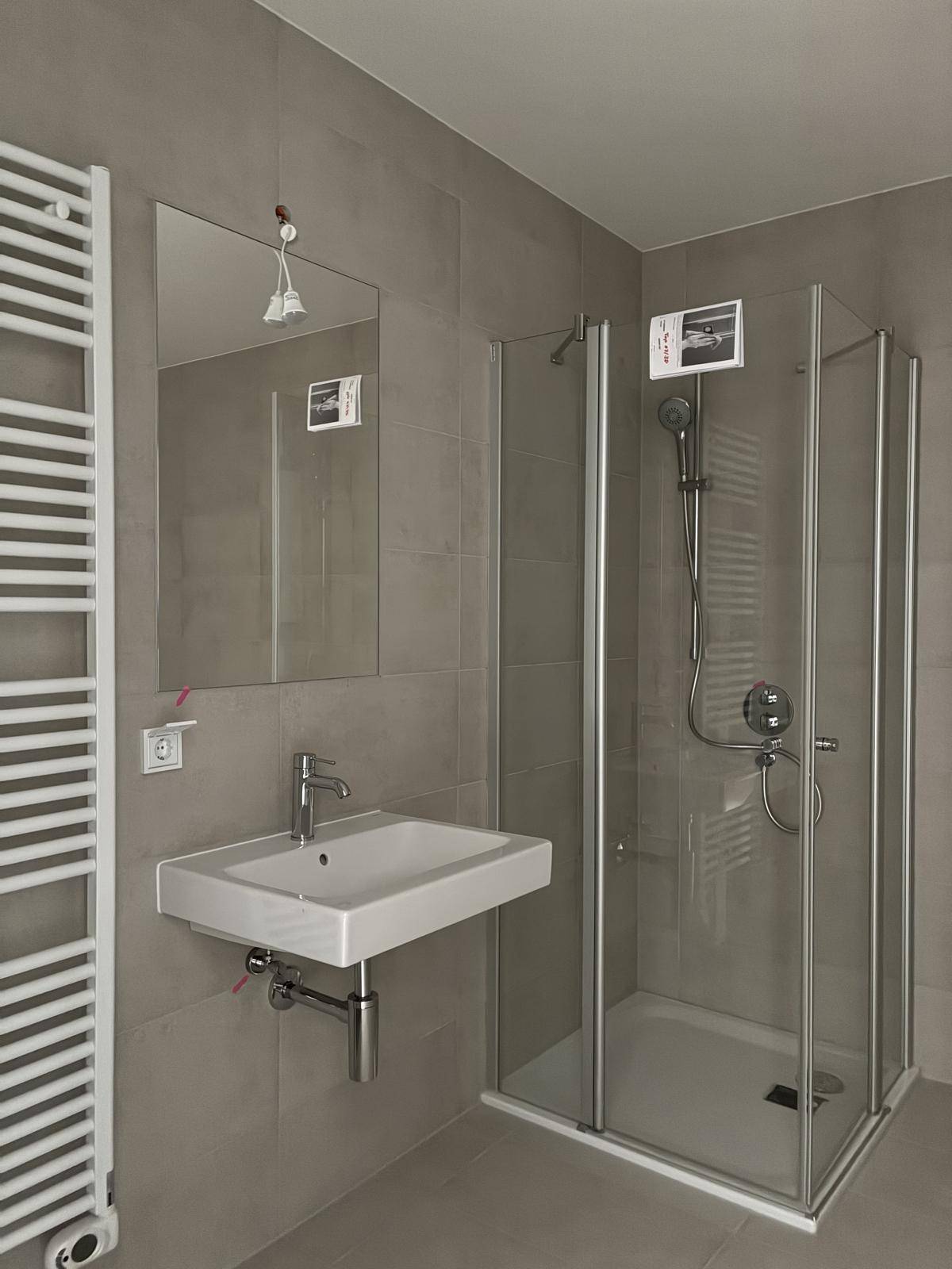 Modernes Badezimmer mit Duschkabine, Waschbecken und beheiztem Handtuchhalter, komplett gefliest.