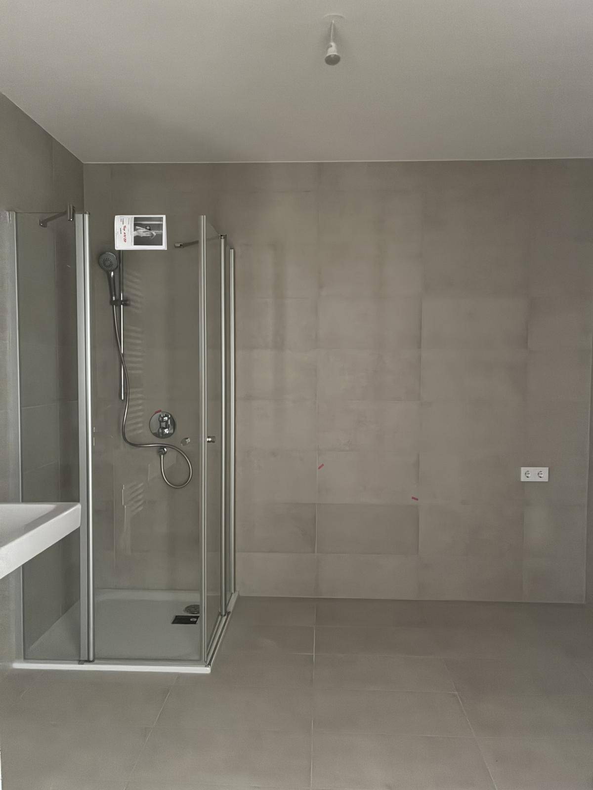Funktionales Badezimmer mit Duschkabine und modernen grauen Fliesen an Wänden und Boden.
