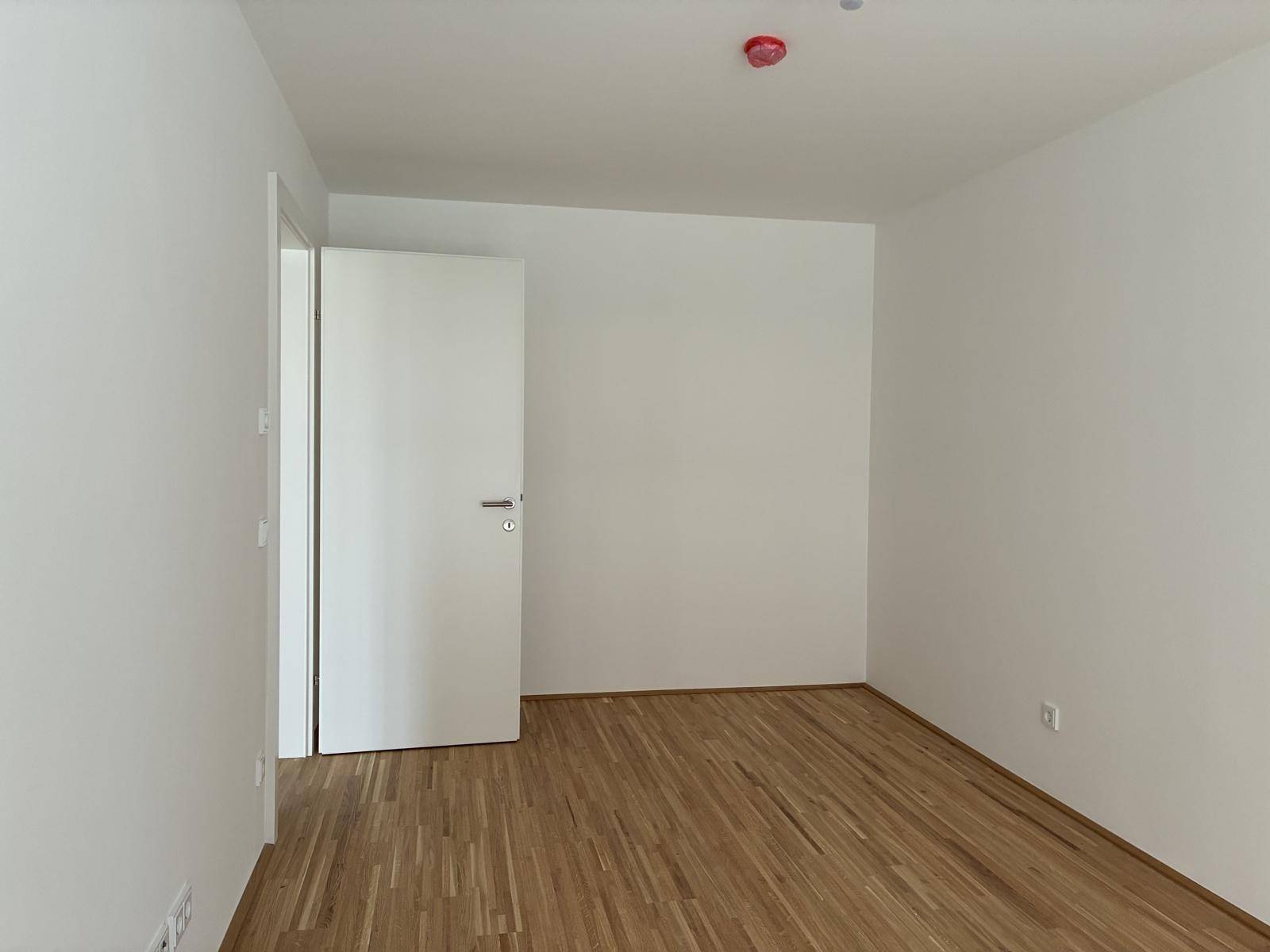 Leeres Zimmer mit Holzboden und weiß gestrichenen Wänden, bereit zum Einzug.