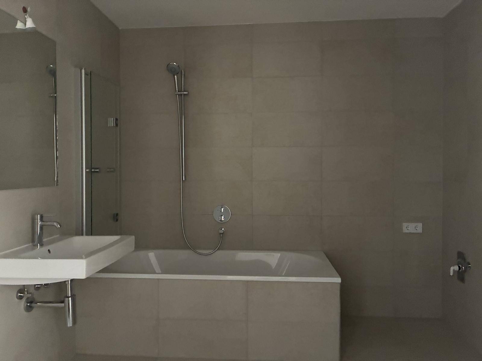 Helles Badezimmer mit Badewanne, Waschbecken und großem Spiegel, komplett gefliest.