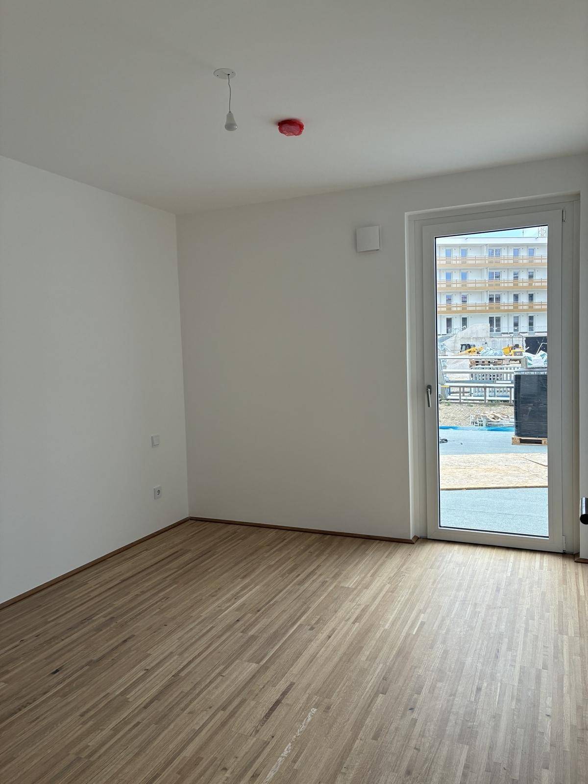 Helles Schlafzimmer mit Holzboden und Zugang zu einem Außenbereich, Blick auf die Baustelle.