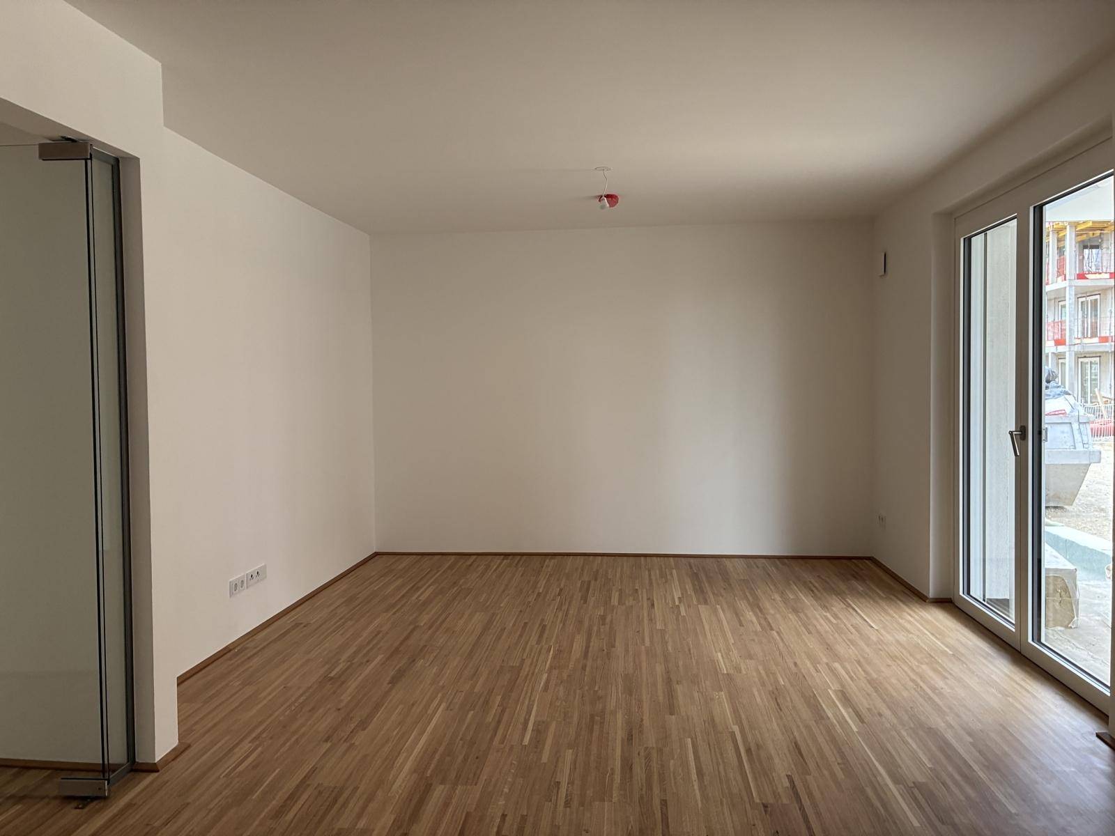 Geräumiger, heller Raum mit Holzboden und Zugang zu einem Außenbereich, ideal für Wohnzwecke.