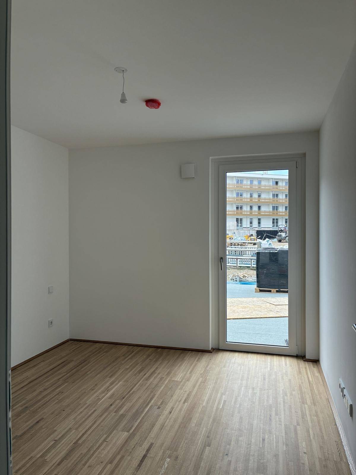 Leeres Schlafzimmer mit Holzboden und Fenster, das viel Tageslicht hereinlässt und einen klaren Blick bietet.