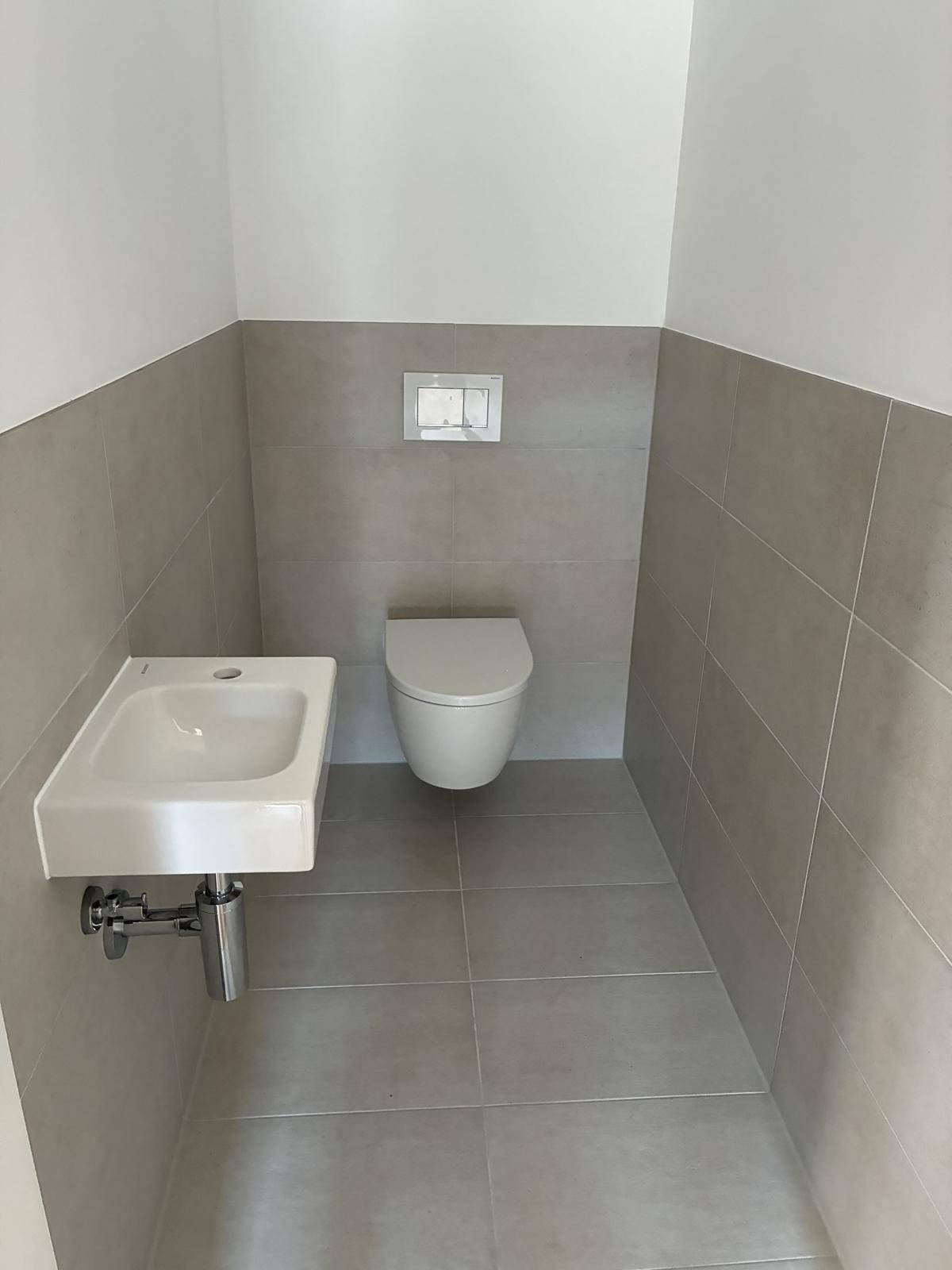 Modernes Gäste-WC mit Wand-WC und kleinem Waschbecken, halbhoch mit hellgrauen Fliesen gefliest.