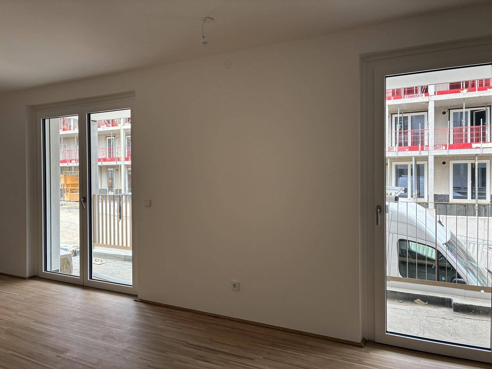 Heller, leerer Raum mit großen Fenstern und Holzboden, der viel Tageslicht hereinlässt.