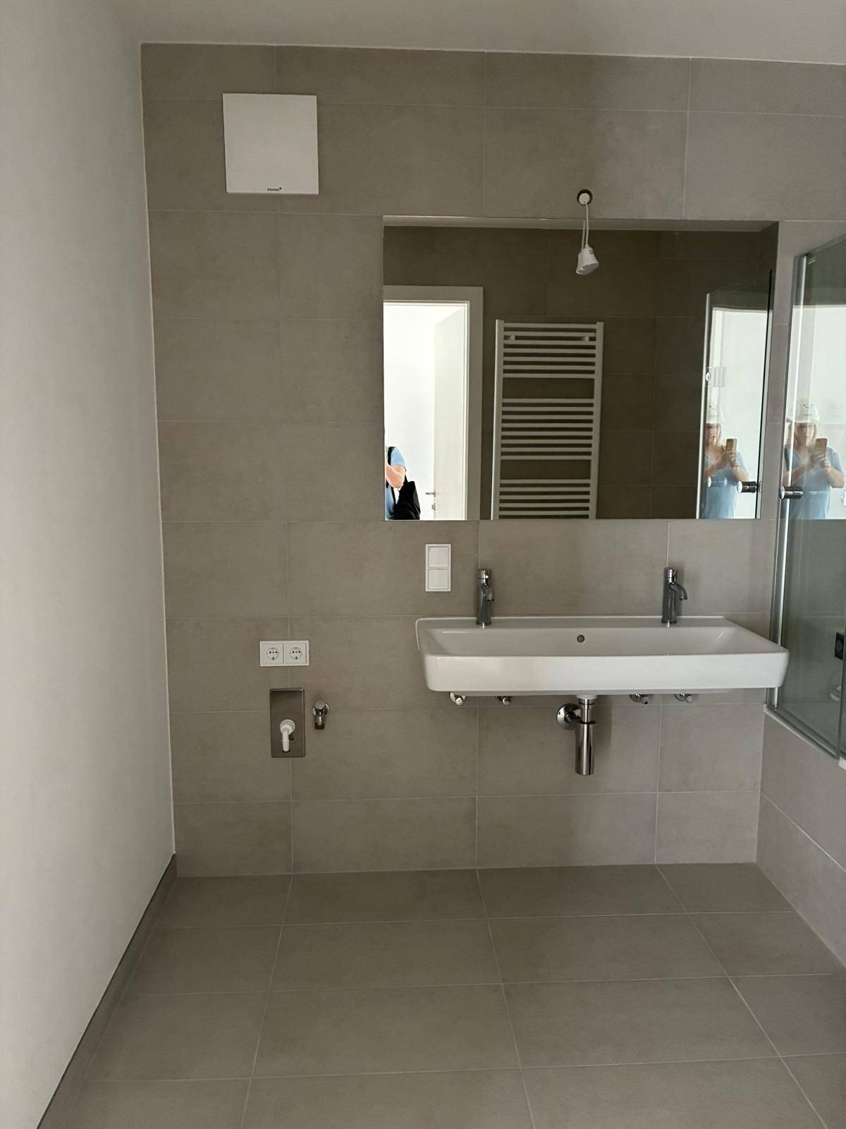 Geräumiges Badezimmer mit Doppelwaschbecken, großem Spiegel und beheiztem Handtuchhalter.