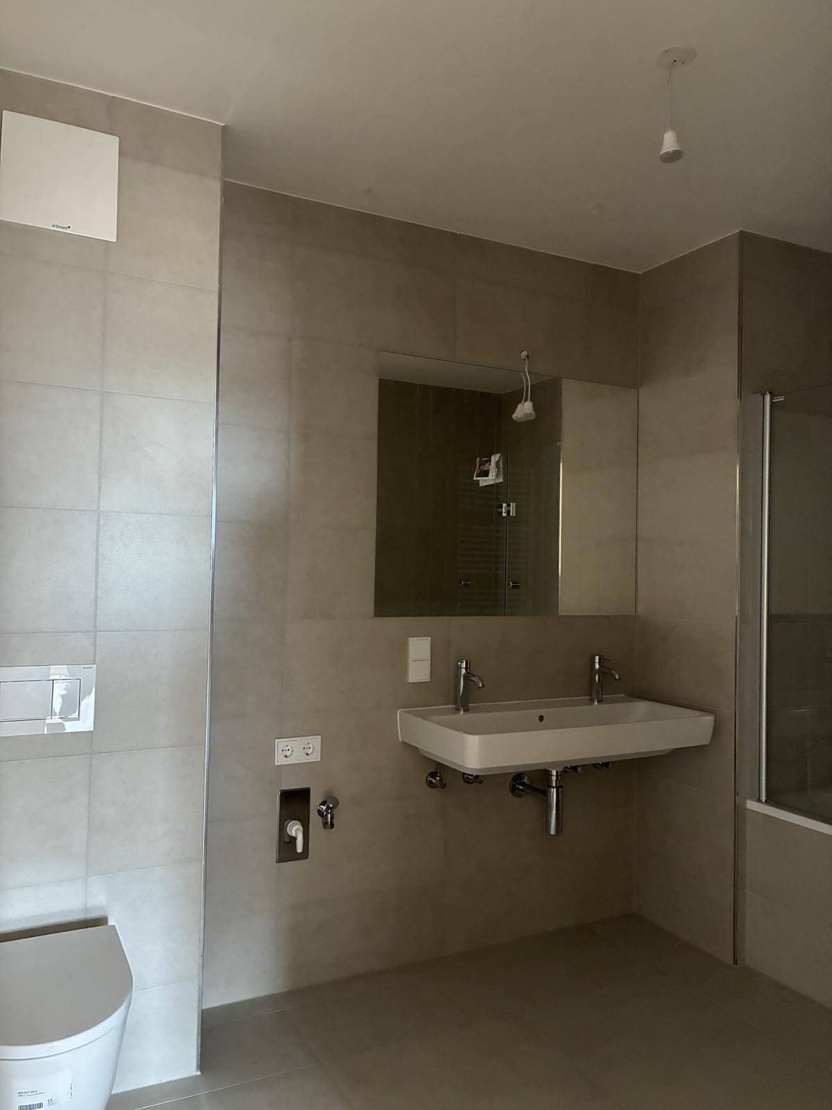 Modernes Badezimmer mit doppelten Waschbecken, Wand-WC und großen Fliesen.