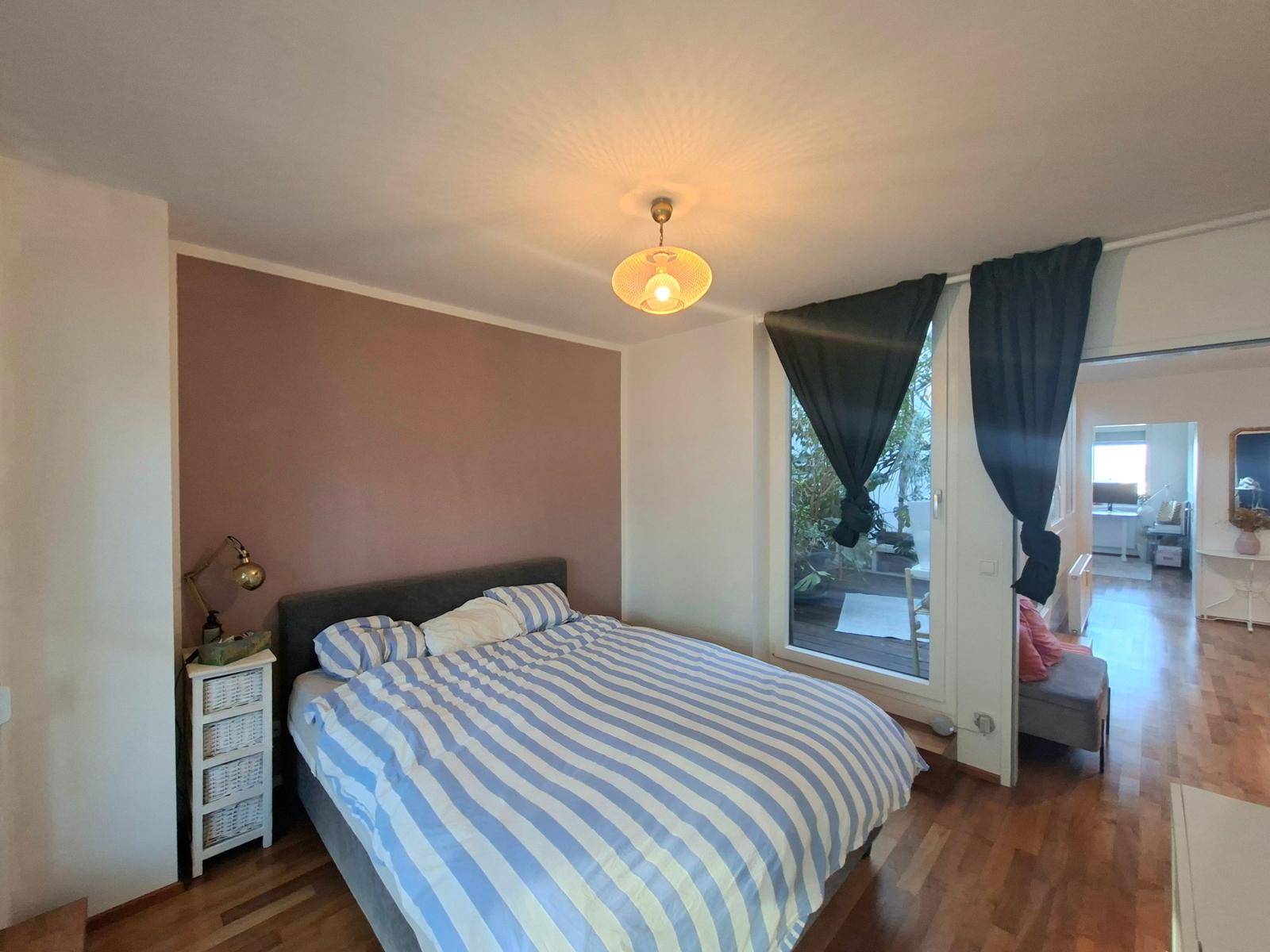 Schlafzimmer mit Doppelbett, Holzboden und Blick auf den angrenzenden Außenbereich.