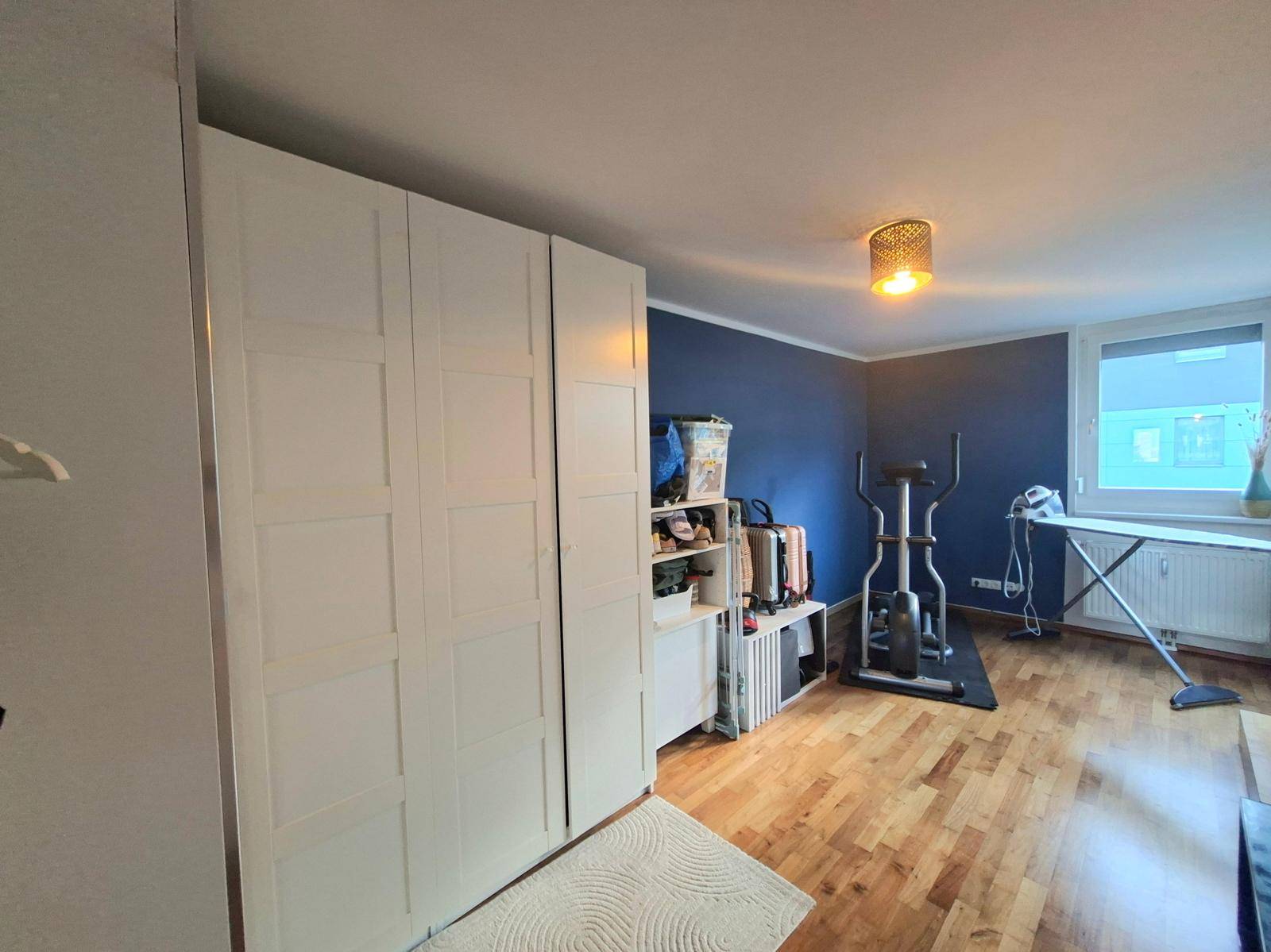 Schlafzimmer mit großem weißen Kleiderschrank, Fitnessgerät und einer blauen Akzentwand.