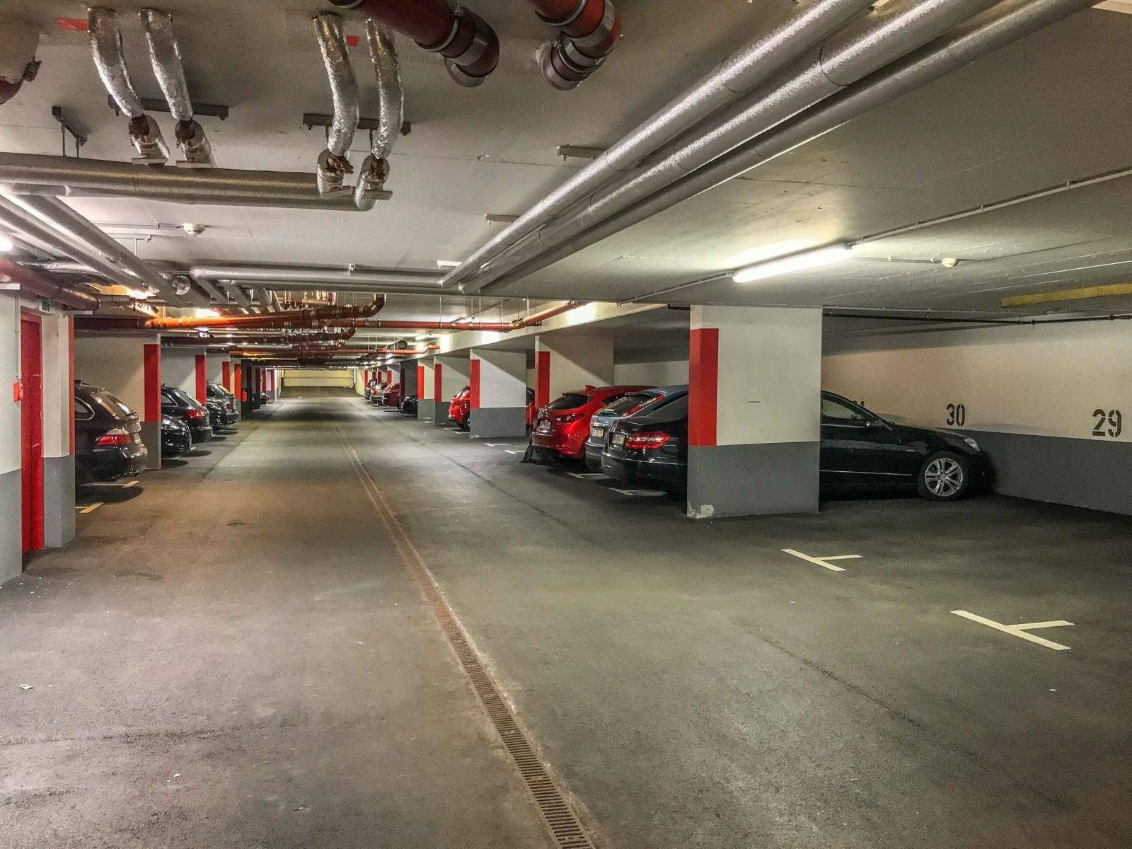 Weitläufige Tiefgarage mit zahlreichen Stellplätzen und sichtbaren Versorgungsleitungen an der Decke.