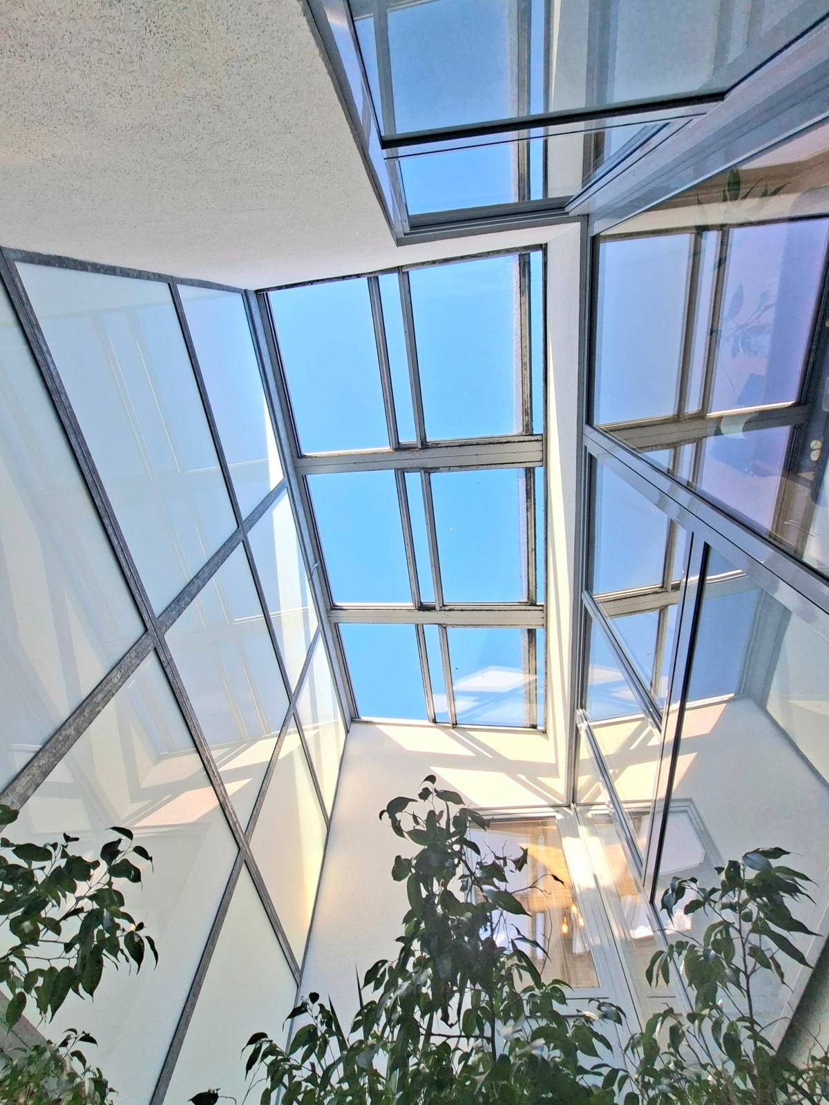 Blick nach oben in einen lichtdurchfluteten Raum mit Glasdach und großen Fenstern.