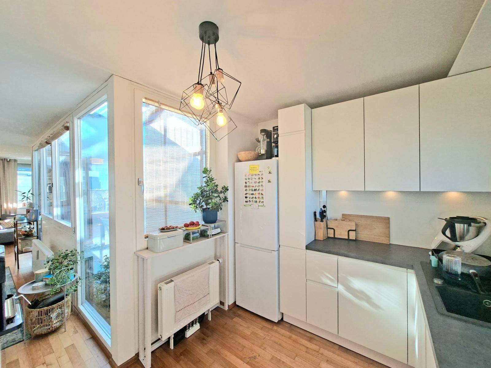 Helle Küche mit weißen Schränken, Kühlschrank und Blick auf den angrenzenden Wohnbereich.