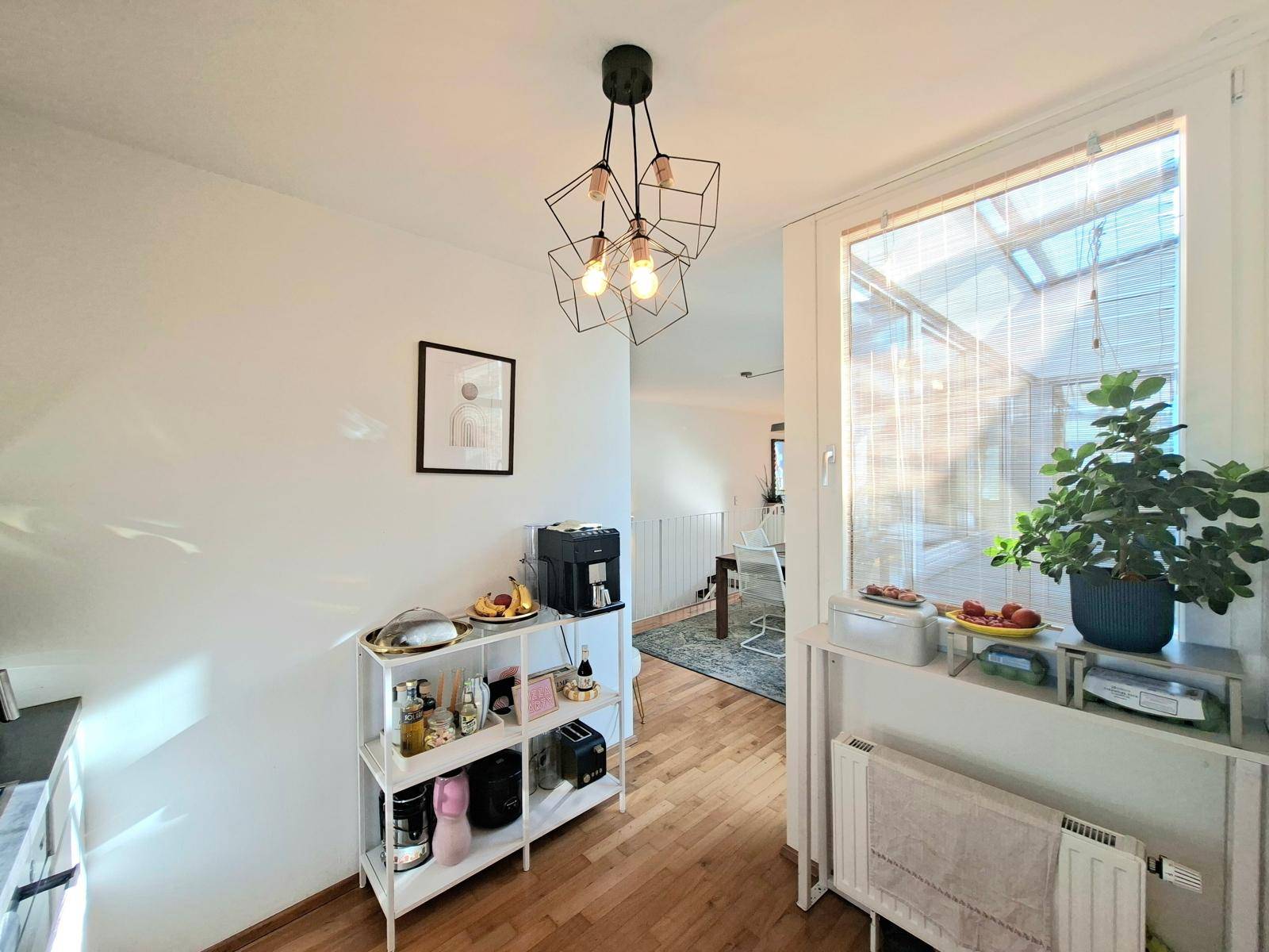 Küchenbereich mit Kaffeemaschine und Regal, der zu einem hellen Wohnraum führt.