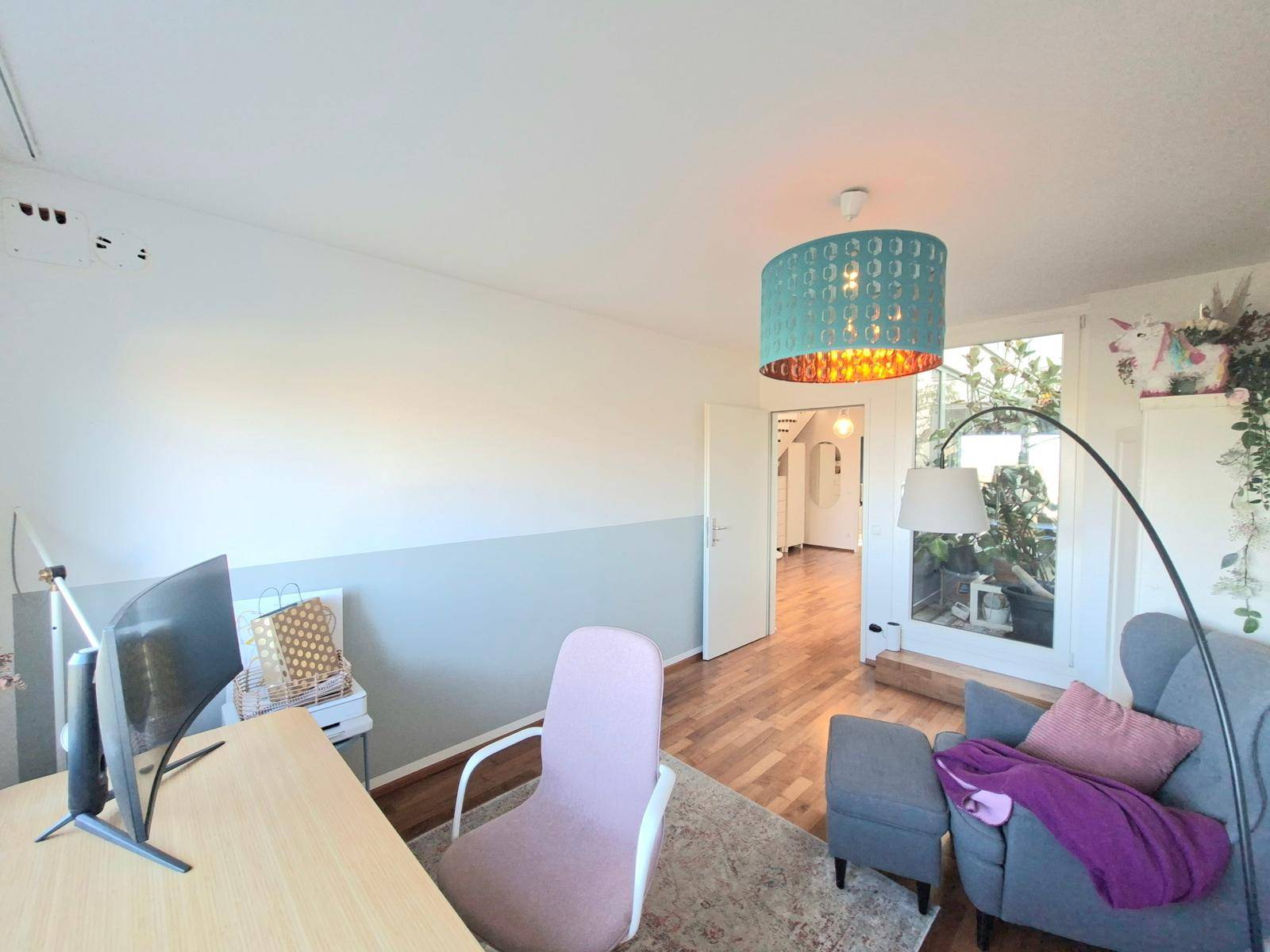 Arbeitszimmer mit Schreibtisch, Sessel und einem Durchgang zu weiteren Wohnbereichen.